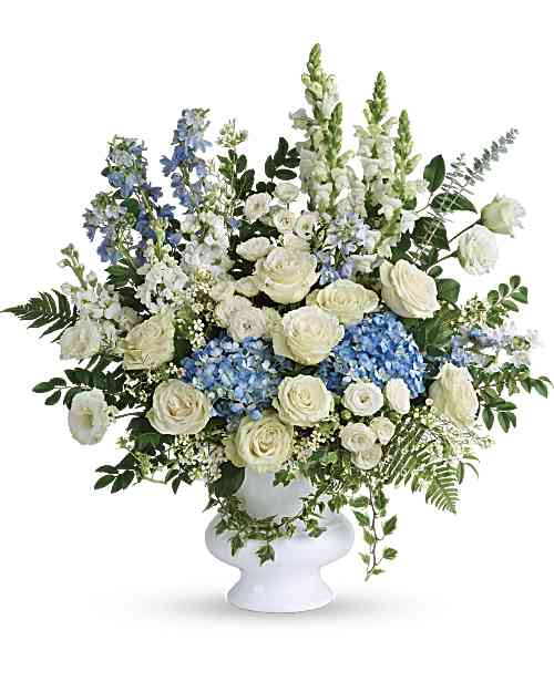 Treasured And Beloved Bouquet - Honor the memory of your beloved with this breathtaking bouquet of sky blue hydrangea and cloud white roses in a classic white urn. This beautiful bouquet of light blue hydrangea, white roses, white spray roses, white lisianthus, light blue delphinium, white snapdragons, white stock, and white waxflower is accented with huckleberry, variegated ivy, spiral eucalyptus, dagger fern, and lemon leaf.