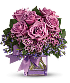 Pink roses in a clear glass vase with a purple ribbon