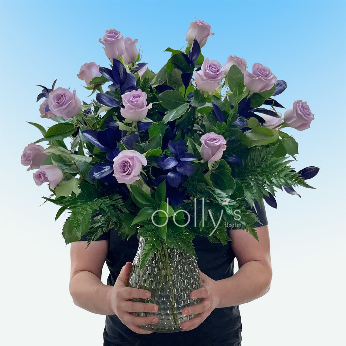 Classic 18 Lavender Long-Stem Roses - Lavender long-stem roses take center stage in this romantic bouquet, their soft lavender petals set against deep purple accent foliage for a rich, elegant contrast perfect for a birthday, anniversary, Valentine's Day, or simply to say "I love you." The kind of arrangement that makes the person you're thinking of feel truly seen and celebrated.  A full, rounded silhouette of 18 long-stem lavender roses is softened by abundant green filler and subtle white accents, arranged to showcase each bloom's graceful shape. Presented in a textured clear glass vase, the design keeps the focus on the flowers while adding a modern, airy finish. Ideal for romantic moments or cheerful surprises, this arrangement arrives ready to display; change the water every 2-3 days, recut stems at an angle, and keep out of direct heat to help the roses last longer.