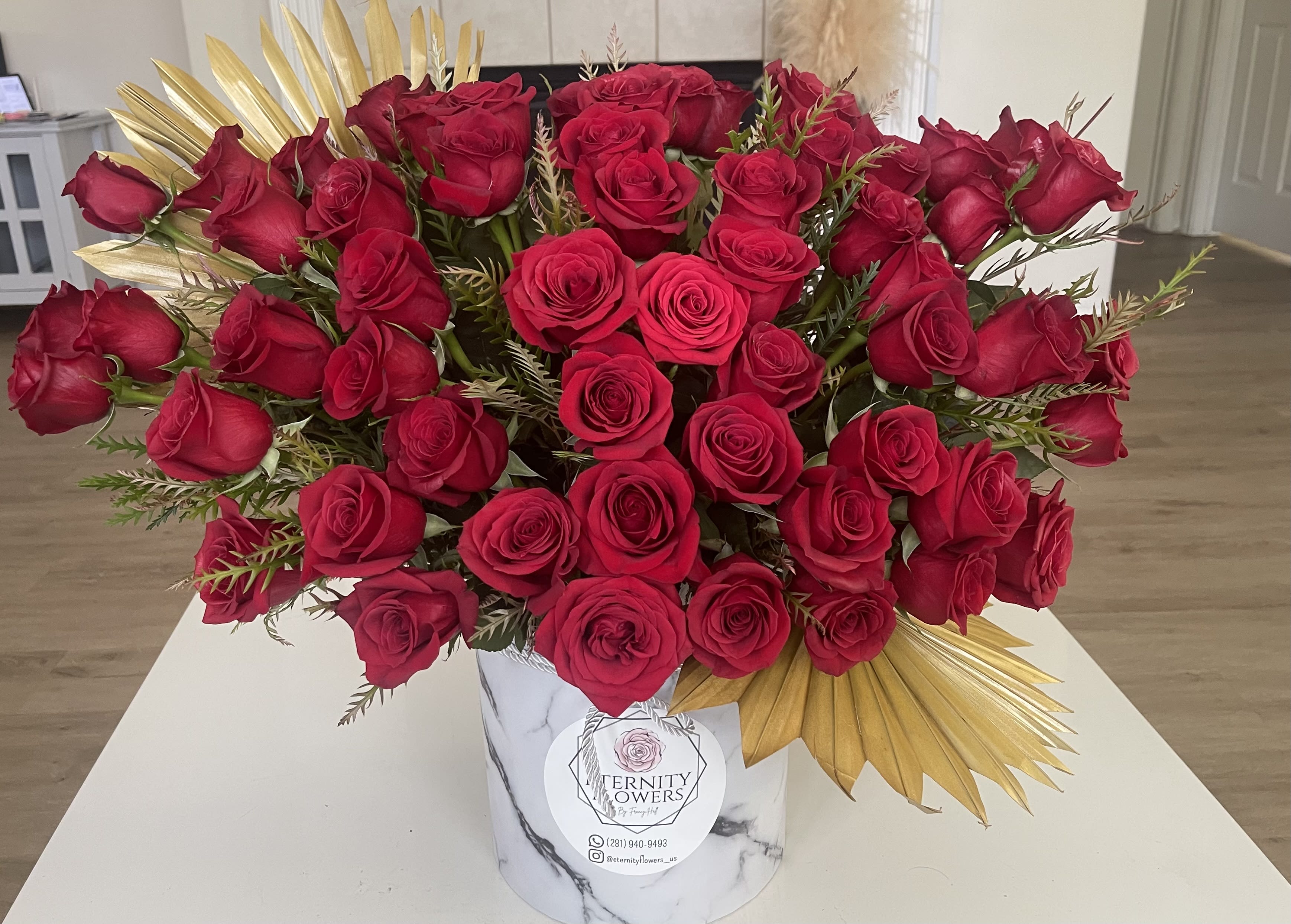 Large bouquet of red roses in a white marble-patterned box with gold accents.