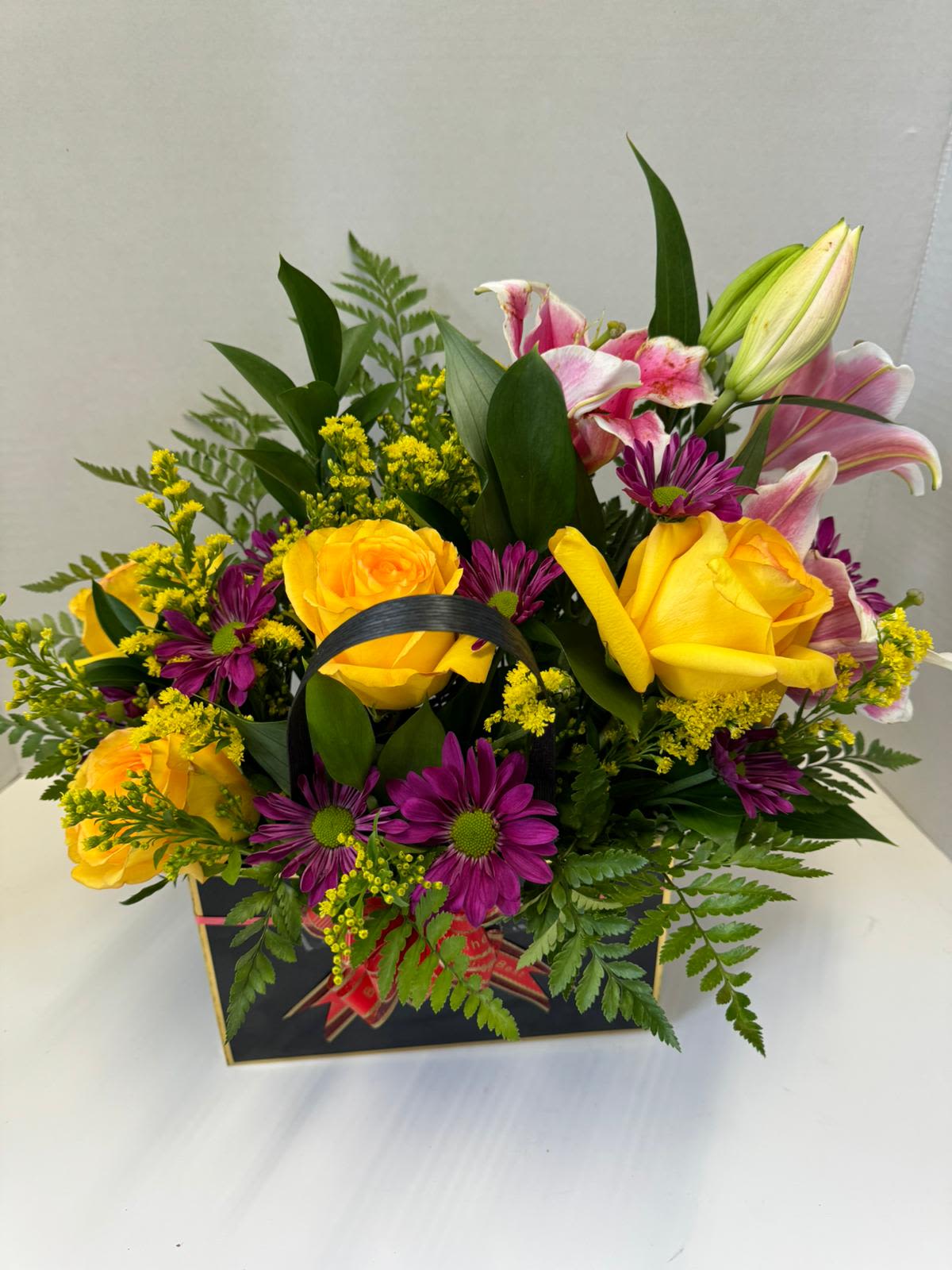 Bouquet of yellow roses, pink lilies, and purple daisies in a gift box