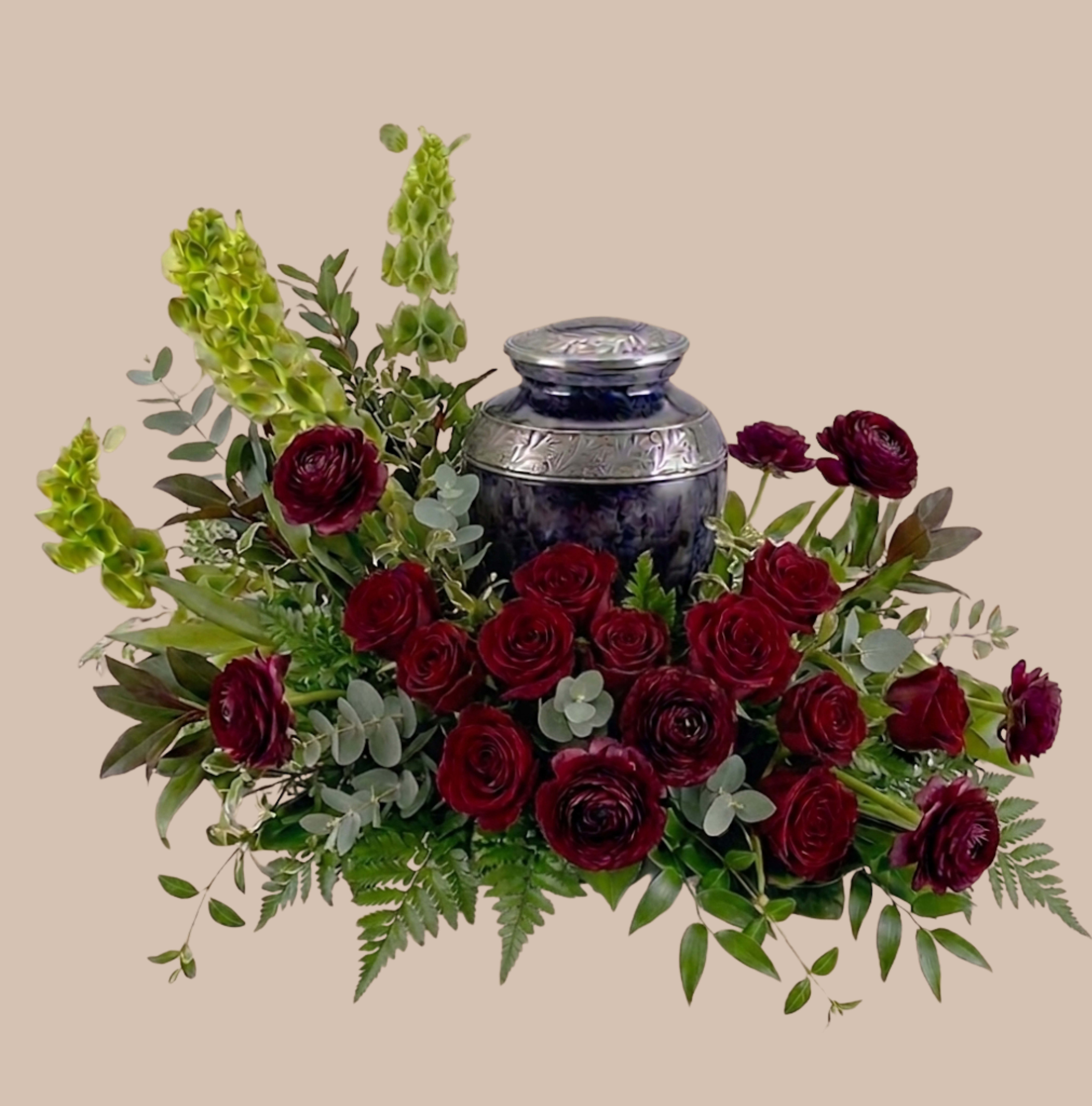 Red Remembrance Tribute - A dense cluster of deep red roses crowns a dark ceramic urn in this Red Remembrance Tribute, a sympathy and funeral arrangement that reads with rich, respectful drama. The burgundy garden roses and spray roses form the visual heart-an elegant, formal statement-while taller green spires and mixed foliage lift the composition, giving it a layered, sculptural silhouette that feels both comforting and dignified.  Alongside the roses you'll find complementary blooms and textures in purple, white, and mixed tones that soften the overall effect and add subtle contrast to the dominant red. Arranged in a decorative dark urn vase, the piece is structured for visibility at a service, memorial table, or as a lasting tribute in the home; its compact, formal shape creates a strong focal point without overwhelming a space.  Designed to honor someone special, this arrangement offers a meaningful way to express sympathy, gratitude, or deep remembrance-the kind of gift that makes the recipient feel truly seen. The ceramic urn provides a stable, display-ready vessel; no additional container is required, and simple fresh water changes will keep blooms looking their best for several days.