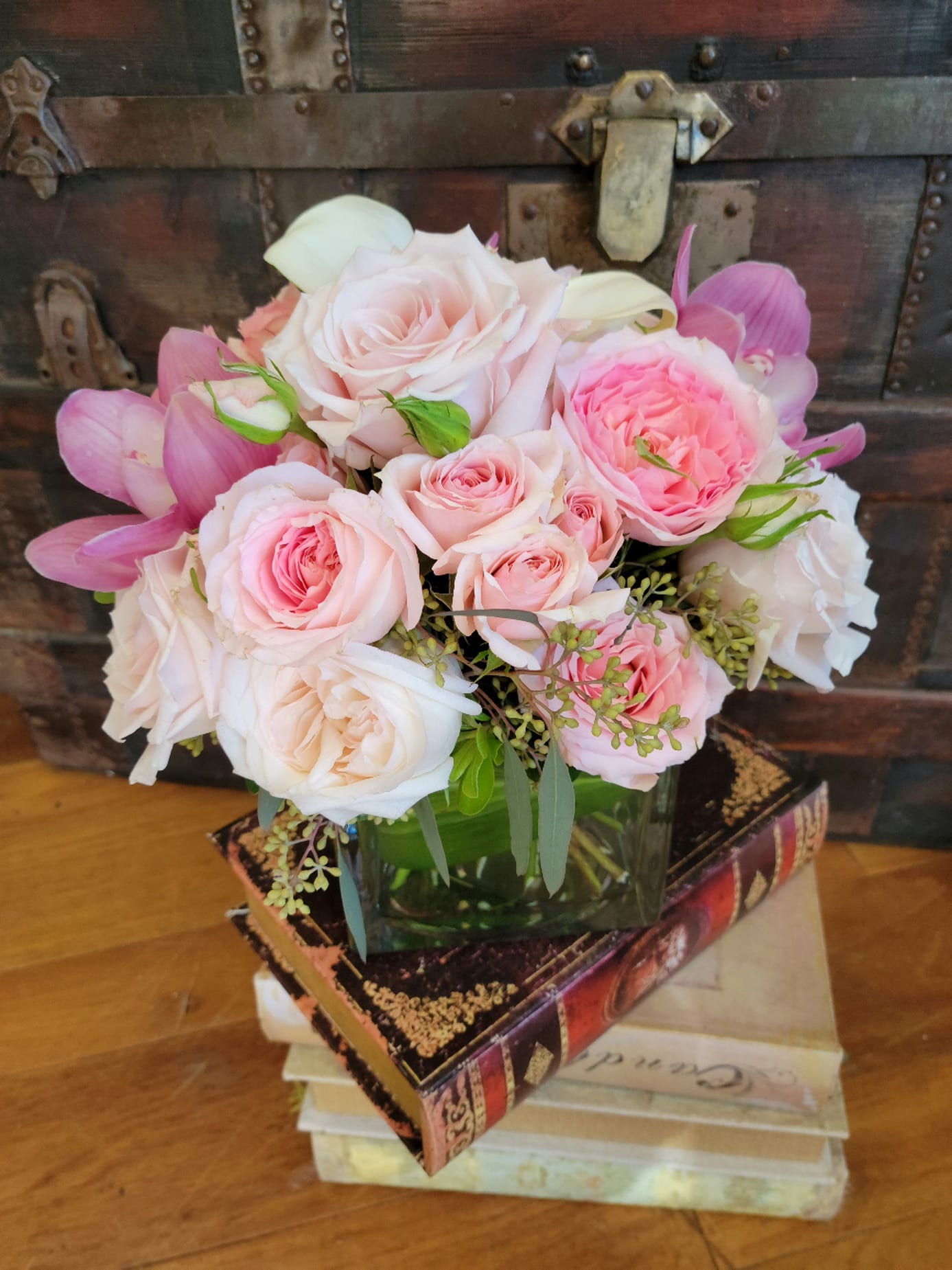 Low arrangement of pale pink roses and white calla lilies in a glass vase on stacked vintage books.