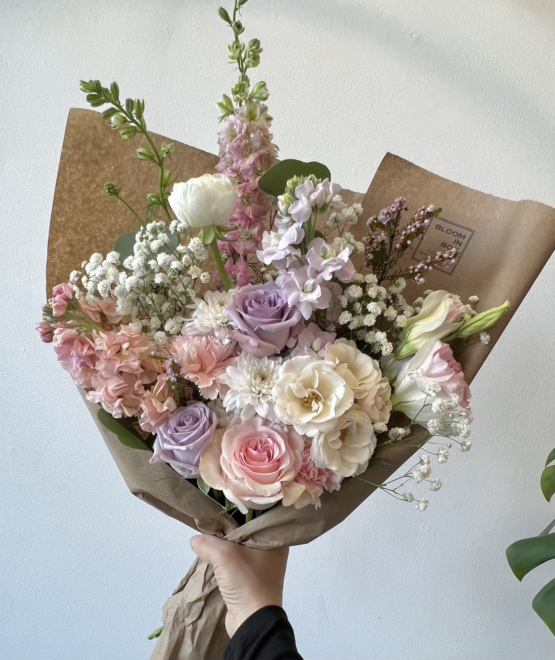Hand-tied bouquet of pastel roses, lisianthus, and baby’s breath in brown paper
