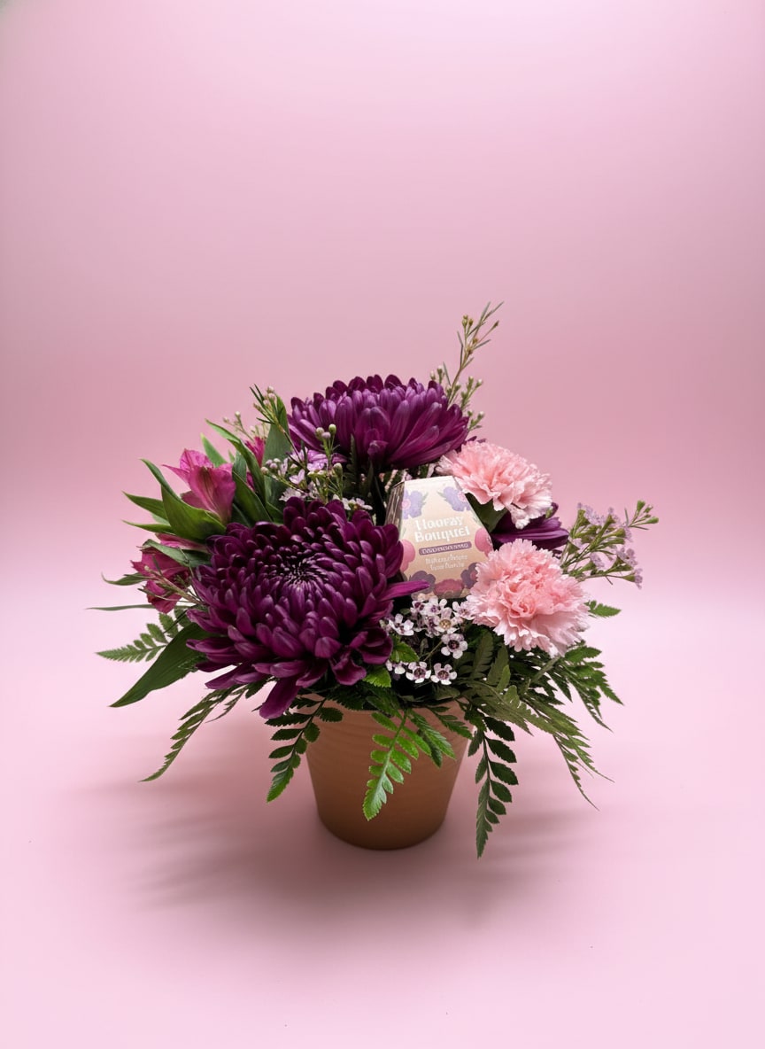 Grow with Love - Grow with Love is a heartfelt floral arrangement designed in a rustic brown melamine container, paired with a wildflower seed packet for a gift that keeps on blooming. Purple cremone mums add rich texture and depth, while light pink carnations and hot pink alstroemeria bring a bright, joyful pop of color. Soft pink waxflower weaves throughout for a delicate, airy finish.  A meaningful blend of fresh flowers and future growth, this design is perfect for birthdays, thank-yous, sympathy, or any moment that calls for a lasting reminder of care and connection.  All flowers, floral colors, and containers are subject to change due to availability.