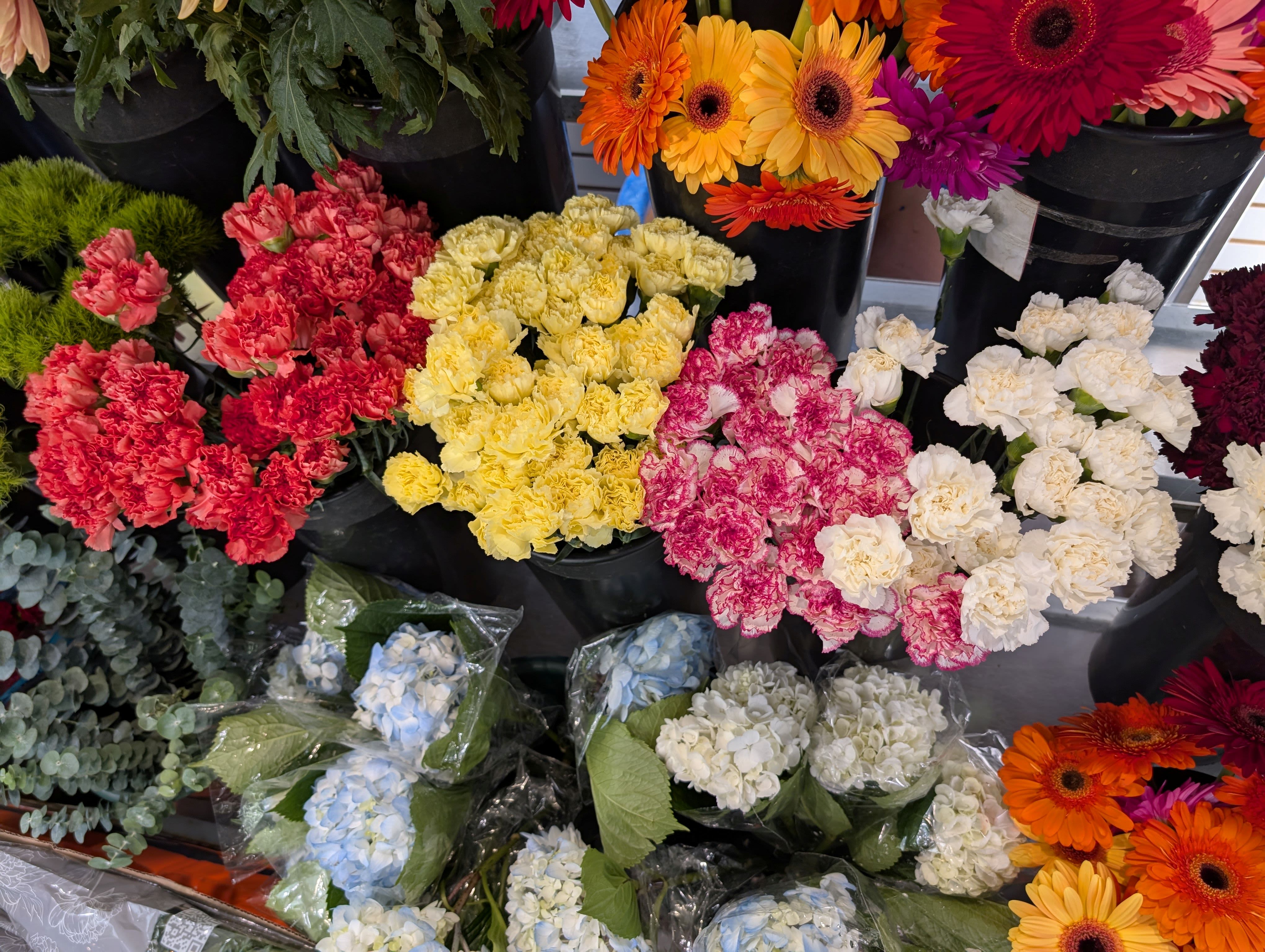 Buckets of colorful carnations and gerbera daisies at a flower market