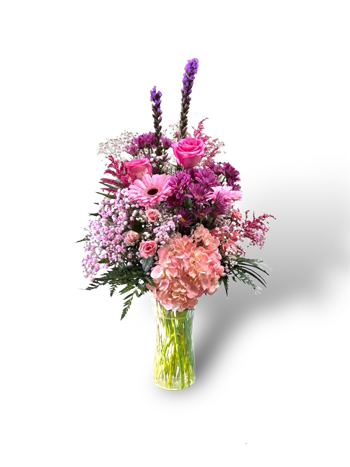 Perfect pink - The "Perfect Pink" arrangement is a beautiful and vibrant floral display presented in a clear glass vase. The arrangement is one-sided, designed to showcase the flowers from the front. It features a stunning combination of lush, full-bloomed pink hydrangeas that bring depth and texture to the bouquet. Nestled among the hydrangeas are delicate daisies, adding a touch of whimsy and lightness. Completing the arrangement are elegant pink roses, which add a touch of romance and sophistication. The overall effect is a charming and eye-catching display, perfect for brightening any room with its fresh, elegant, and romantic appeal.