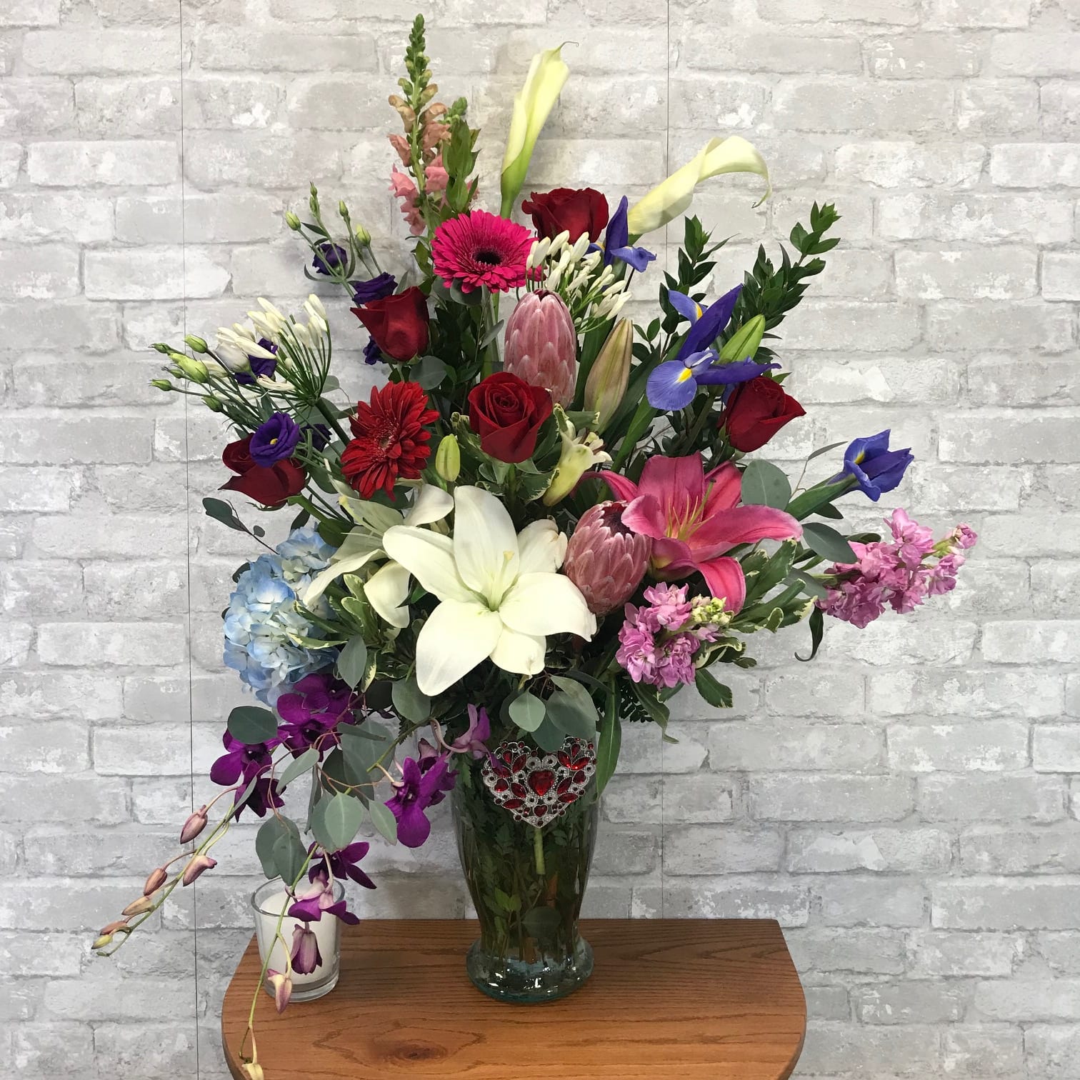 I'm Yours FG221 - This is a regal design with amazing premium flowers including several roses. It is a one sided arrangement with a beautiful crystal heart accenting the vase.  This gift would overwhelm the receiver.    Approximately 36" H and 30" W.