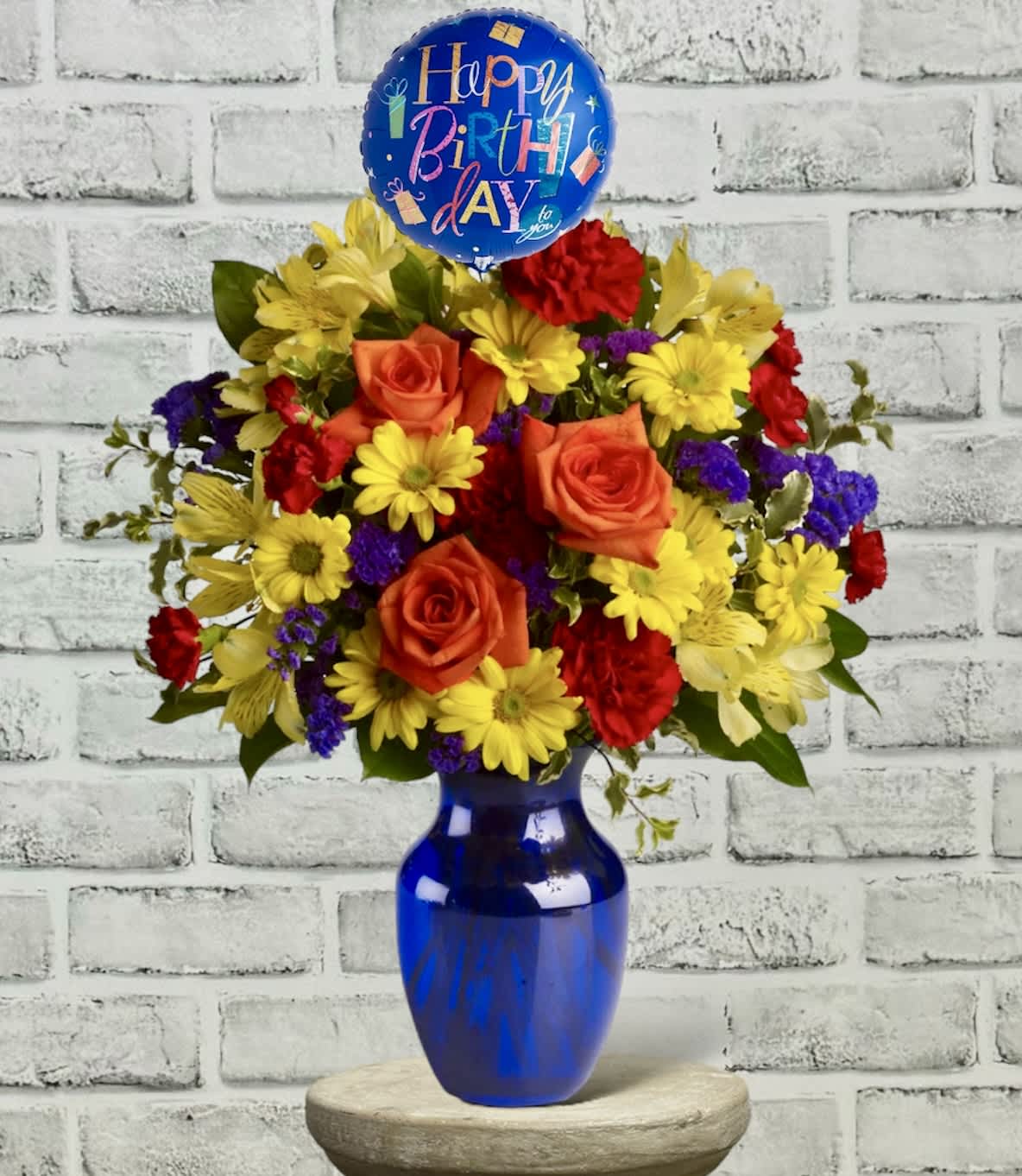 Birthday bouquet with roses and daisies in a blue vase, topped with a balloon