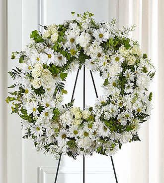 White floral wreath on a black stand with daisies and roses