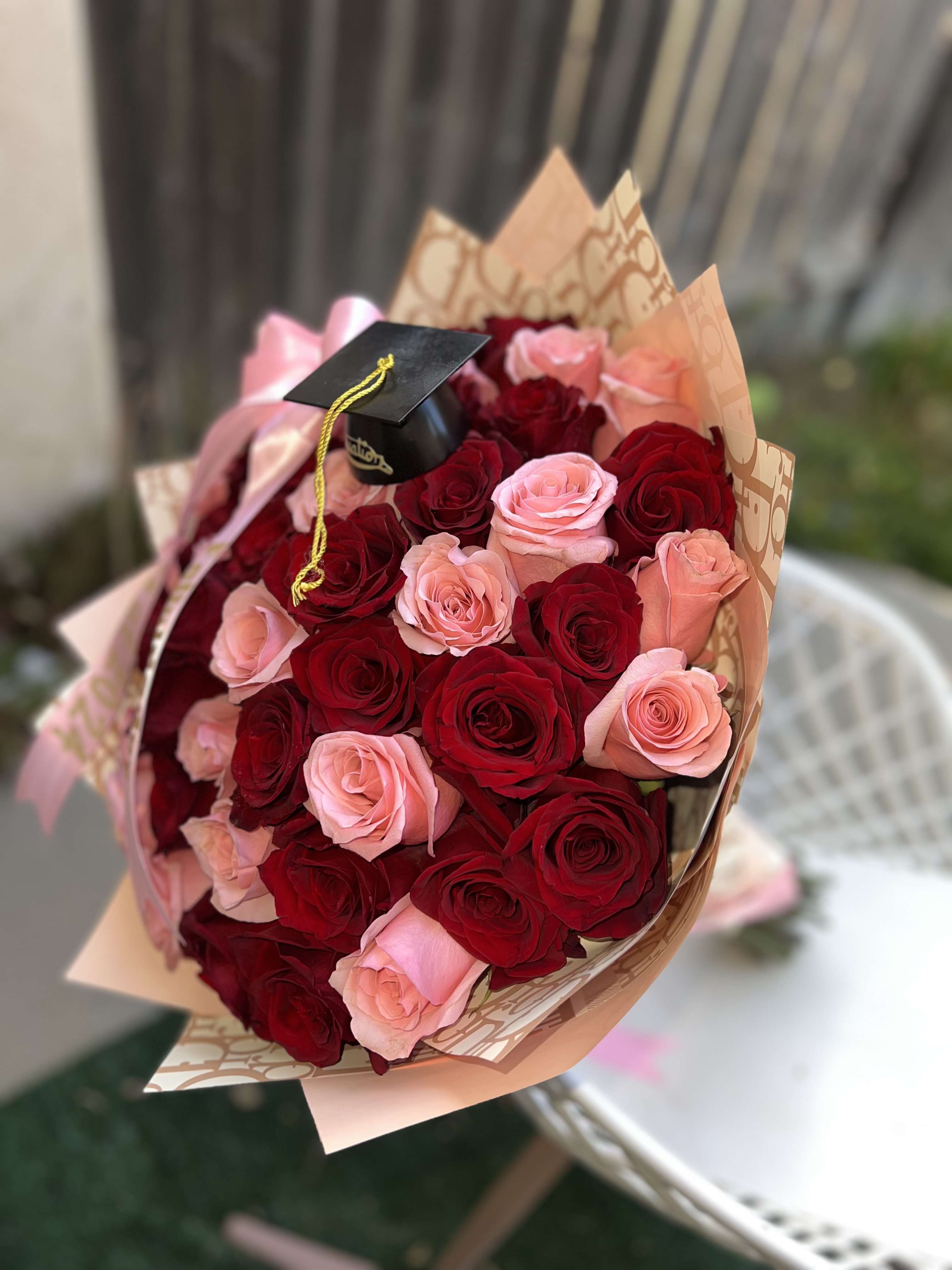 Grad Bouquet - Celebrate this proud moment with elegance and charm. this graduation bouquet features lush, velvety red roses-symbolizing love, respect, and admiration. finished with matching ribbon, and optional graduation topper, this bouquet makes the perfect congratulatory gift to honor a special graduate's hard work and bright future.  