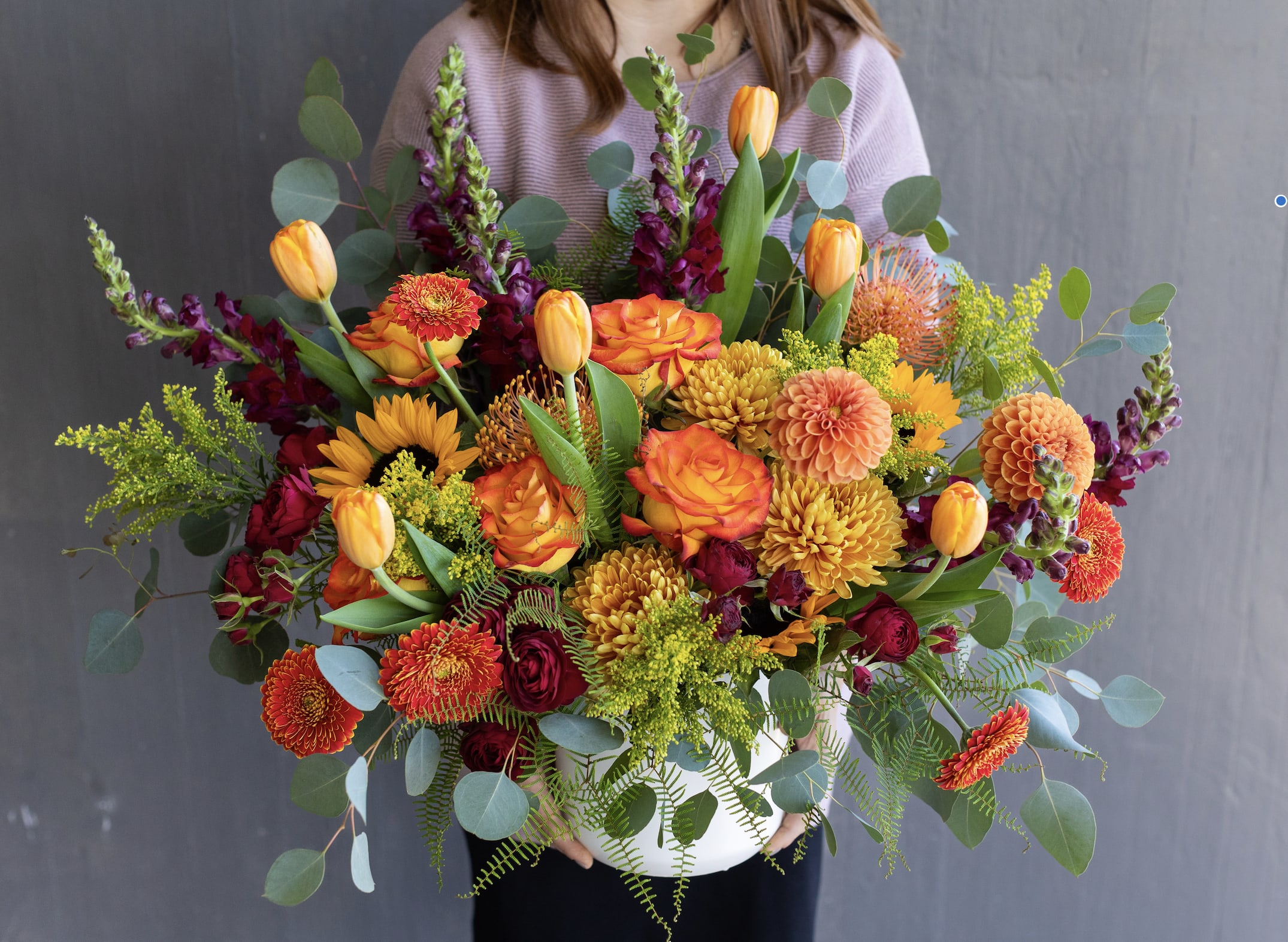 Large bouquet of orange, yellow, and burgundy flowers in a white vase