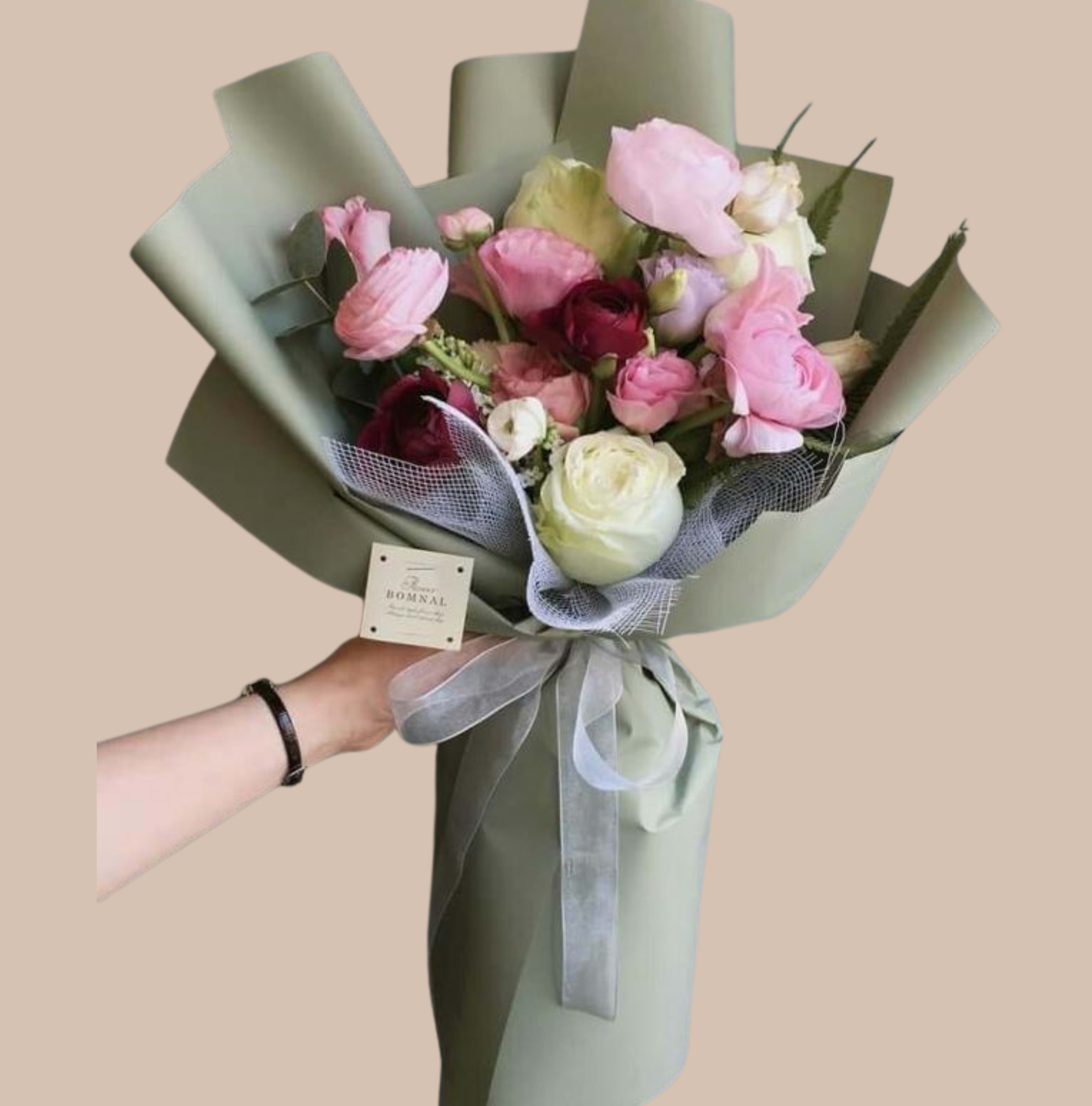Rose &amp; Wrapped - Lush, layered peony blooms in soft pink, creamy white, and deeper magenta create a romantic, hand-tied flower arrangement perfect for a birthday bouquet, anniversary gift, or a thoughtful everyday surprise. The rounded, abundant shape and textural contrast between the full peony heads and fresh greenery make the recipient feel warmly noticed-the kind of bouquet that reads as both elegant and genuinely personal.  Wrapped in taupe and white paper with a dark brown satin ribbon and branded tag, this arrangement has a polished, modern presentation that still feels natural and unfussy. Colors include pink, white, purple and green accents; flowers are centered on full peonies with lush foliage. Sized as a hand-tied bouquet, it arrives ready to display in a vase or to present as-is; to keep blooms looking their best, recut stems and change water daily after delivery.