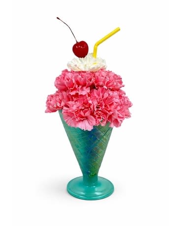 Birthday Summer Milkshake - Bright pink carnations piled into a turquoise cone-shaped glass create an instant smile - this playful flower arrangement is a birthday bouquet perfect for anyone who loves whimsical, novelty gifts. Designed to read like a summery milkshake, the pink blooms are topped with a white whipped-cream accent, finished with a bright red cherry and a yellow straw, so the recipient will feel delighted and celebrated the moment they see it.  The arrangement uses tightly clustered pink carnations for a full, candy-colored look, set in a turquoise glass cone vase that adds a retro, cheerful pop. The white topping provides contrast and texture, while the red cherry and yellow straw deliver the finishing, playful details. Colors include pink, blue (turquoise), white and red for a bold, festive palette that photographs beautifully.  Perfect for birthdays, summer parties, or to cheer someone up with a lighthearted surprise, this piece sends a fun, joyful message rather than a formal one. The compact cone vase makes it easy to display on a desk, countertop, or small table; order with confidence for same-day delivery options when available to make their day extra special.