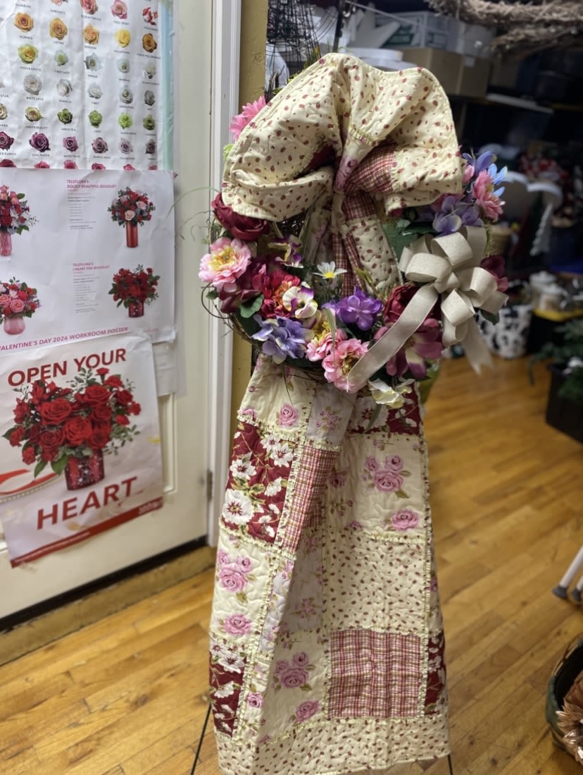 Pink Primitive Throw with Coordinating Silk Grapevine Wreath - A lush cluster of pink, purple, white and red blooms creates a cheerful, romantic statement - perfect as a decorative flower arrangement or a thoughtful gift for Mother's Day, a birthday, or to brighten a home for spring. This floral wreath and coordinating silk grapevine design reads handmade and welcoming; the large cream fabric bow with a patterned center gives it a rustic, primitive charm that draws the eye and signals a personal, handmade touch to the person you're thinking of.  The wreath is built on a circular form and densely covered with mixed bouquets of roses, daisies and orchids, layered for a full, textured look across the lower half while leaving the upper portion to showcase the soft fabric bow and ribbon. Pink and purple tones mingle with crisp white and splashes of red, so the piece reads lively from a distance yet reveals delicate petals and mixed textures up close. Hard goods include the wreath form, coordinating fabric bow and ribbon, and a silk grapevine base for lasting, low-maintenance display.  This is the kind of arrangement that makes someone feel seen - a cozy, decorative accent for a front door, entryway or mantel that says "you matter" without being overformal. Because it uses silk grapevine and fabric accents, it arrives ready to hang and enjoy with no watering required; choose the size that fits your space and order soon to ensure timely delivery for the occasion.