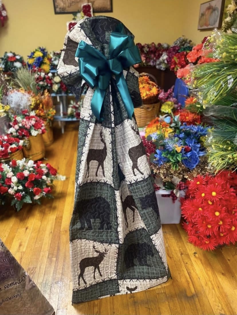 Deer Quilted Throw - A tall, wrapped floral gift with a cozy, rustic vibe-perfect as a seasonal gift or a cheerful housewarming arrangement. This flower arrangement for autumn or holiday giving combines mixed bouquets of carnations and chrysanthemums in mixed color palettes (blue, red, white and warm accents) and is presented upright for easy display; the patchwork-style fabric wrap with deer motifs and a teal satin bow creates a handcrafted, festive impression that will make the recipient feel warmly remembered.  Inside the decorative fabric wrap you'll find layers of textured blooms-frilly carnations and full chrysanthemums-arranged to show off their bright reds, cool blues, crisp whites and complementary seasonal tones. The satin bow tops the piece for an elegant finishing touch and the tall, wrapped presentation makes it ready to set on a entry table or beside a cozy chair. Order now for a gift that reads thoughtful and seasonal; because of its upright design, simple fresh-water care (replace water frequently and trim stems) will keep the flowers looking their best.