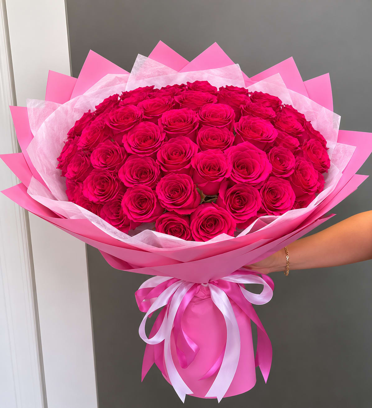 100 Wrap Of pink Roses - A lavish dome of 100 tightly packed pink roses creates an immediate impression of abundance and romance - perfect as an anniversary bouquet, a Valentine's or Mother's Day gift, or a showstopping birthday surprise. The rich range of pinks from soft blush to deep magenta gives depth and movement across the round, hand-wrapped arrangement so the person you're sending it to will feel truly celebrated the moment they see it.  Each rose is arranged in a dense, textured surface and framed with a pale bouquet wrap that keeps the focus on bloom after bloom of long-lasting petals. The wrap makes it easy to carry or present at a party, graduation, housewarming, or holiday gathering, and the compact dome measures and styles like a classic hand-tied bouquet for display in a favorite vase. Ideal for occasions from "just because" and get well wishes to weddings, retirements, or saying "I'm sorry," this is the kind of bouquet that reads as thoughtful, romantic, and luxurious - the sort of gift that makes the recipient feel truly seen.