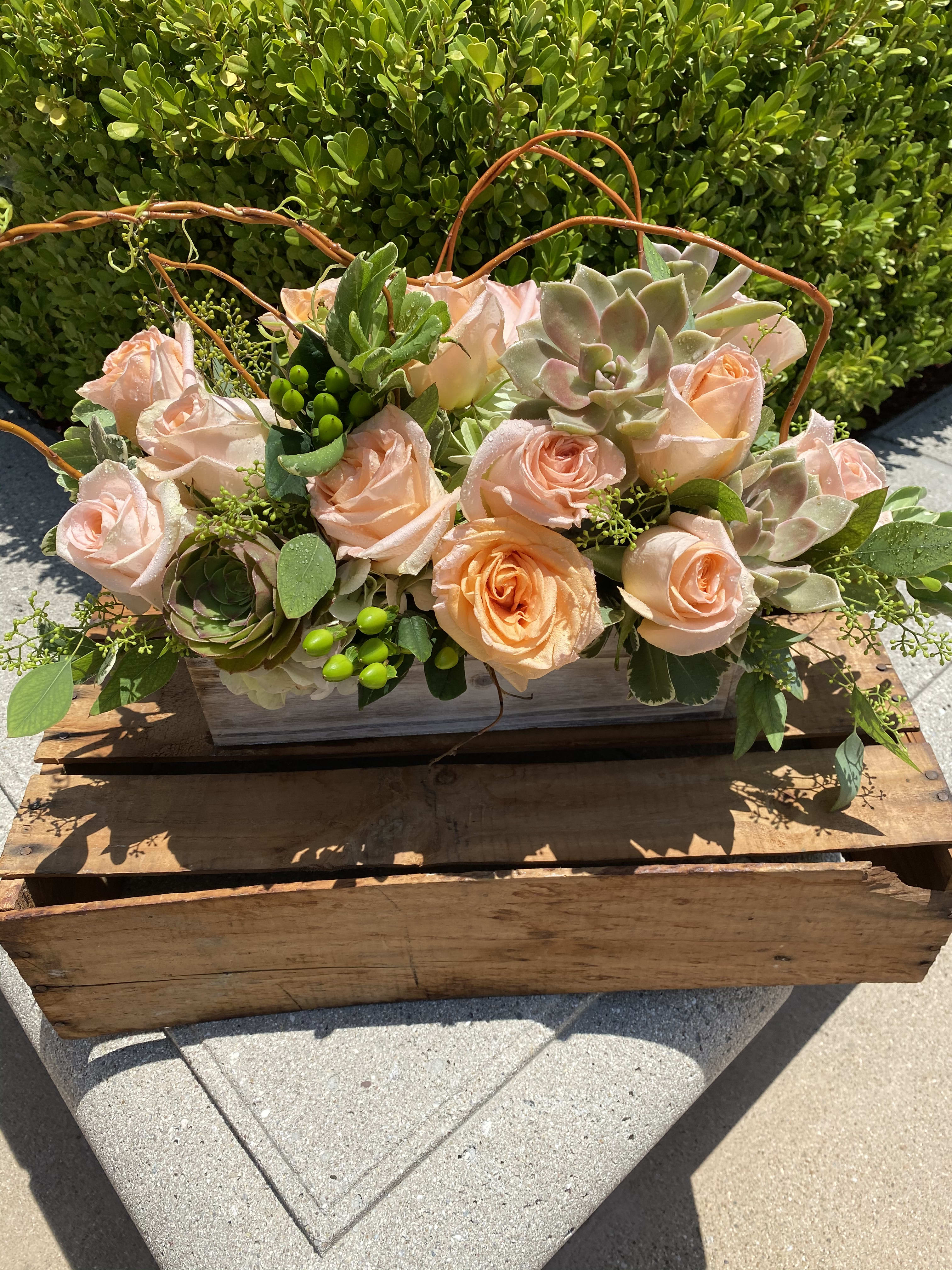 Peach roses and succulents arranged in a wooden box with curved twig handles