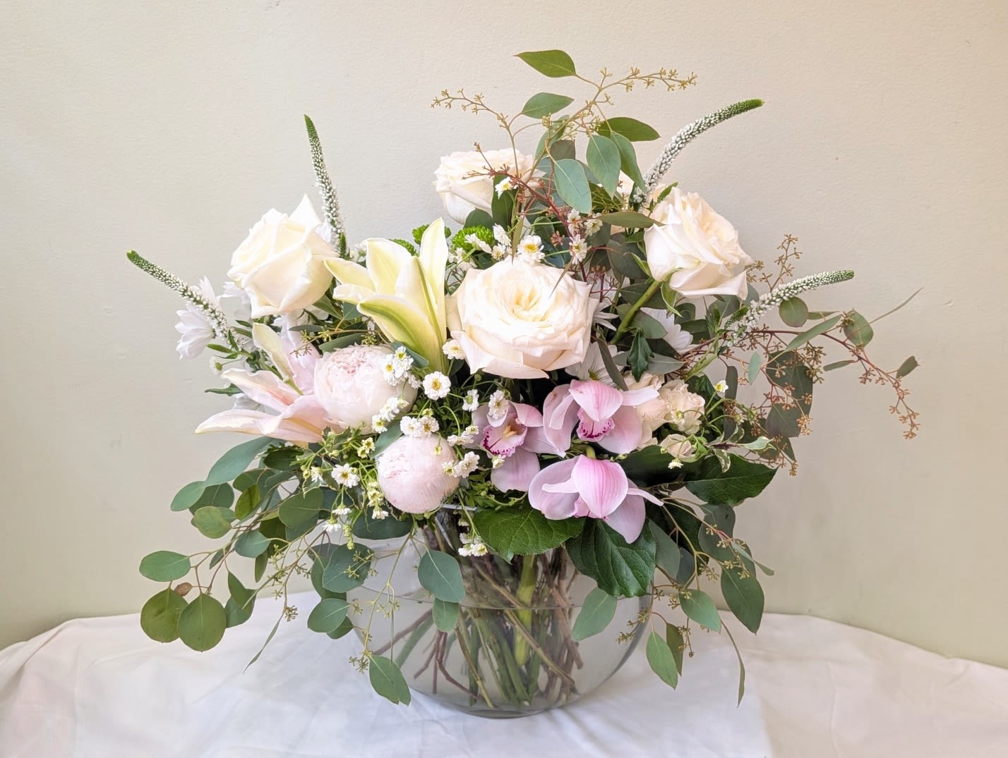 Blush Serenity - Blush Serenity is a graceful and elegant arrangement designed with white and blush pink roses, orchids, lilies, and daisies, complemented by airy branching greenery. Arranged in a low crescent-shaped vase, it adds a touch of natural beauty and refined charm to any room.