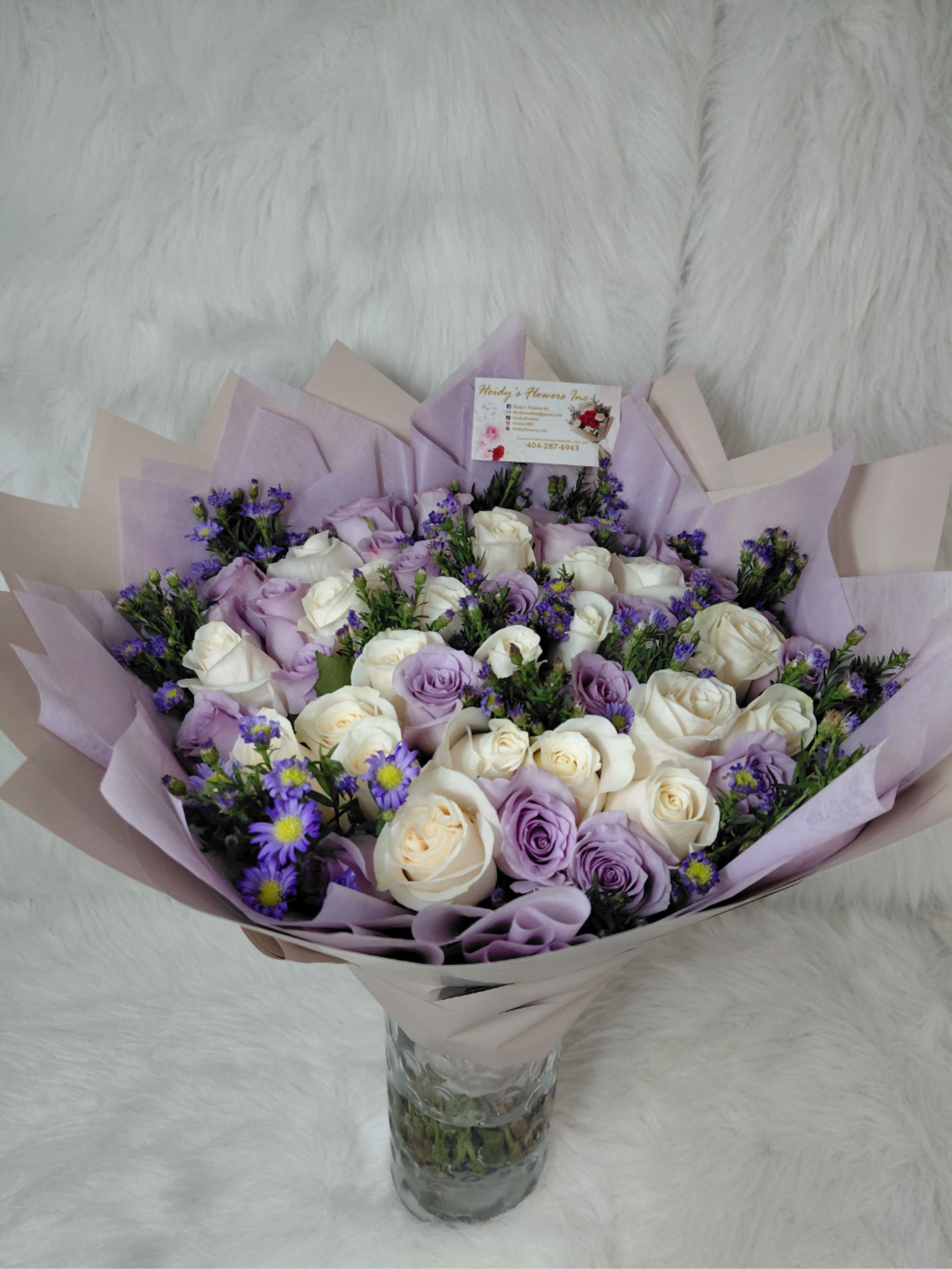 A lavender, bouquet - A cloud of lavender and white roses creates an immediate sense of calm and romance - the perfect anniversary bouquet or just-because surprise for the person you want to make feel truly cherished. This flower arrangement blends tightly packed lavender and white roses with small purple aster-like fillers to give a soft, layered look that reads as both elegant and affectionate; it also works beautifully for birthdays, weddings, Valentine's Day, or to say "I love you" in a memorable way.  Arranged in a clear glass vase and wrapped in pastel lavender and blush paper, the bouquet presents a polished, gift-ready silhouette with cool pastel tones and a full, rounded shape. Gold-wrapped Ferrero Rocher chocolates are thoughtfully tucked among the blooms for an extra touch of celebration, and the package includes kraft and floral tags plus a florist business card for personalization. Sized and finished to feel substantial on a dining table or bedside, this arrangement arrives ready to display - change the water every two days, trim stems slightly at an angle if needed, and keep away from direct heat to prolong freshness.