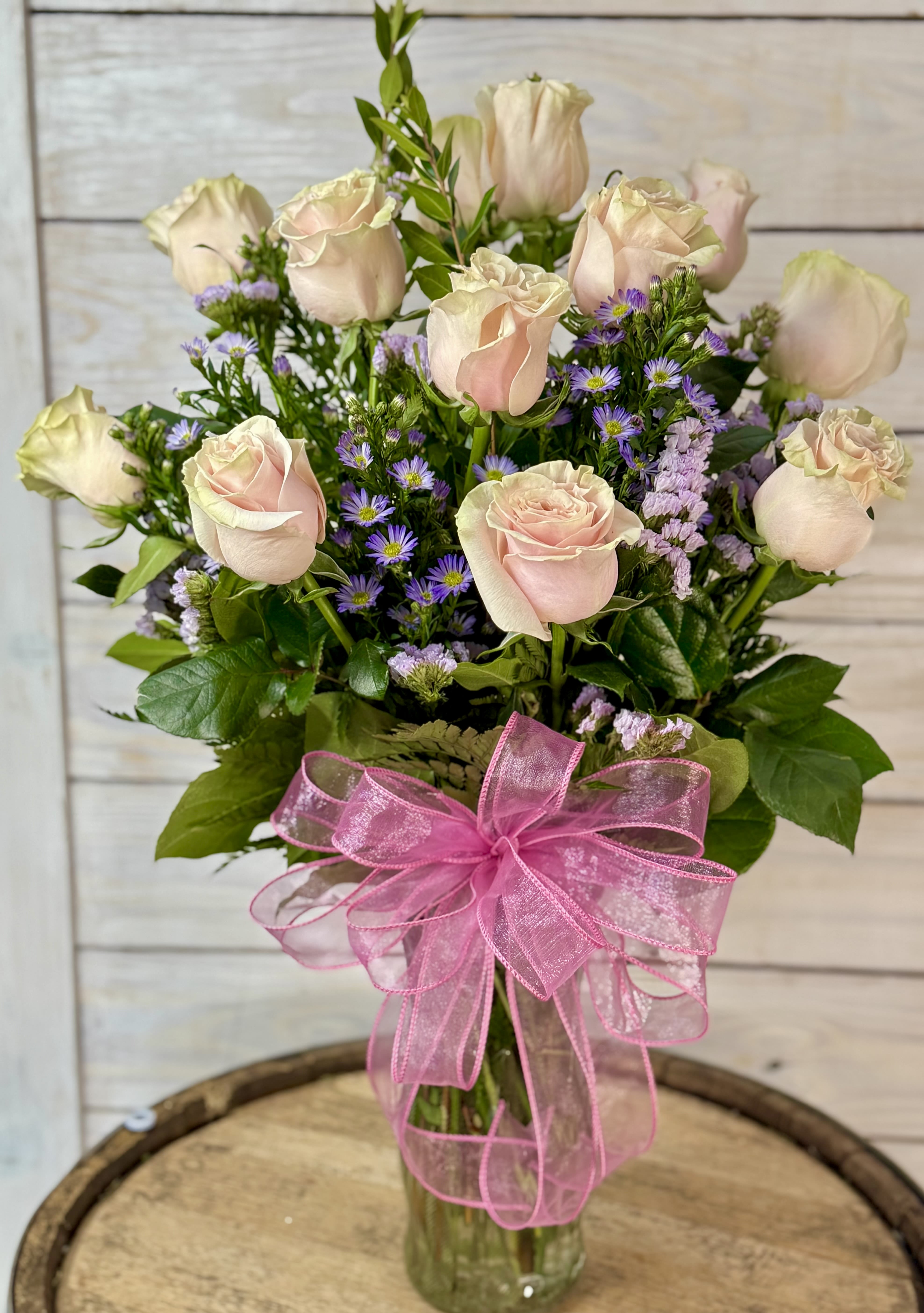 Bouquet of pale pink roses and purple filler flowers in a glass vase with a pink ribbon
