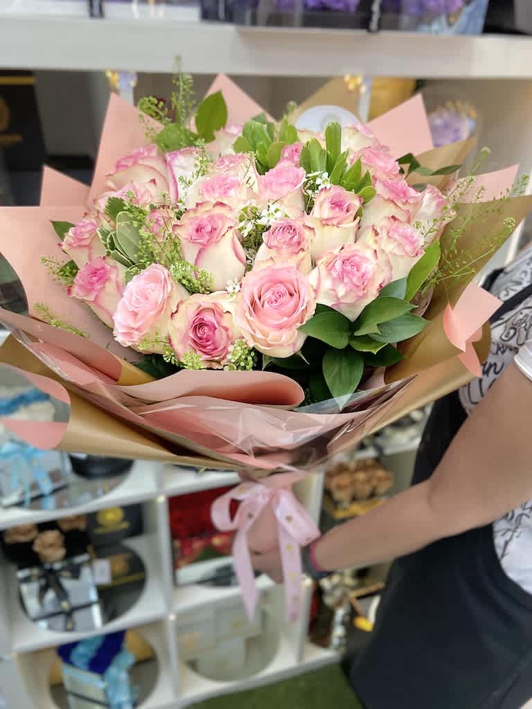 Large hand-tied bouquet of pink and white roses wrapped in pink paper with a satin ribbon bow.