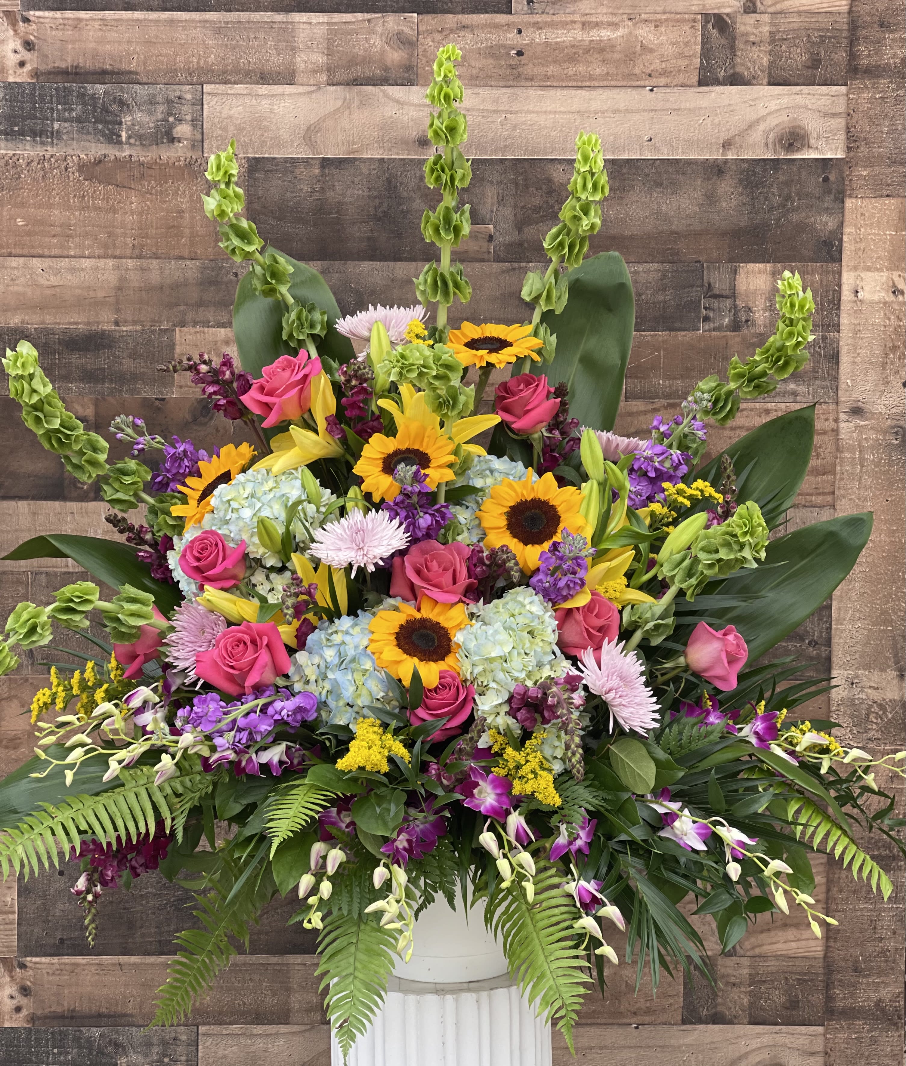 Large mixed bouquet with sunflowers, pink roses, lilies, and hydrangeas in a white vase