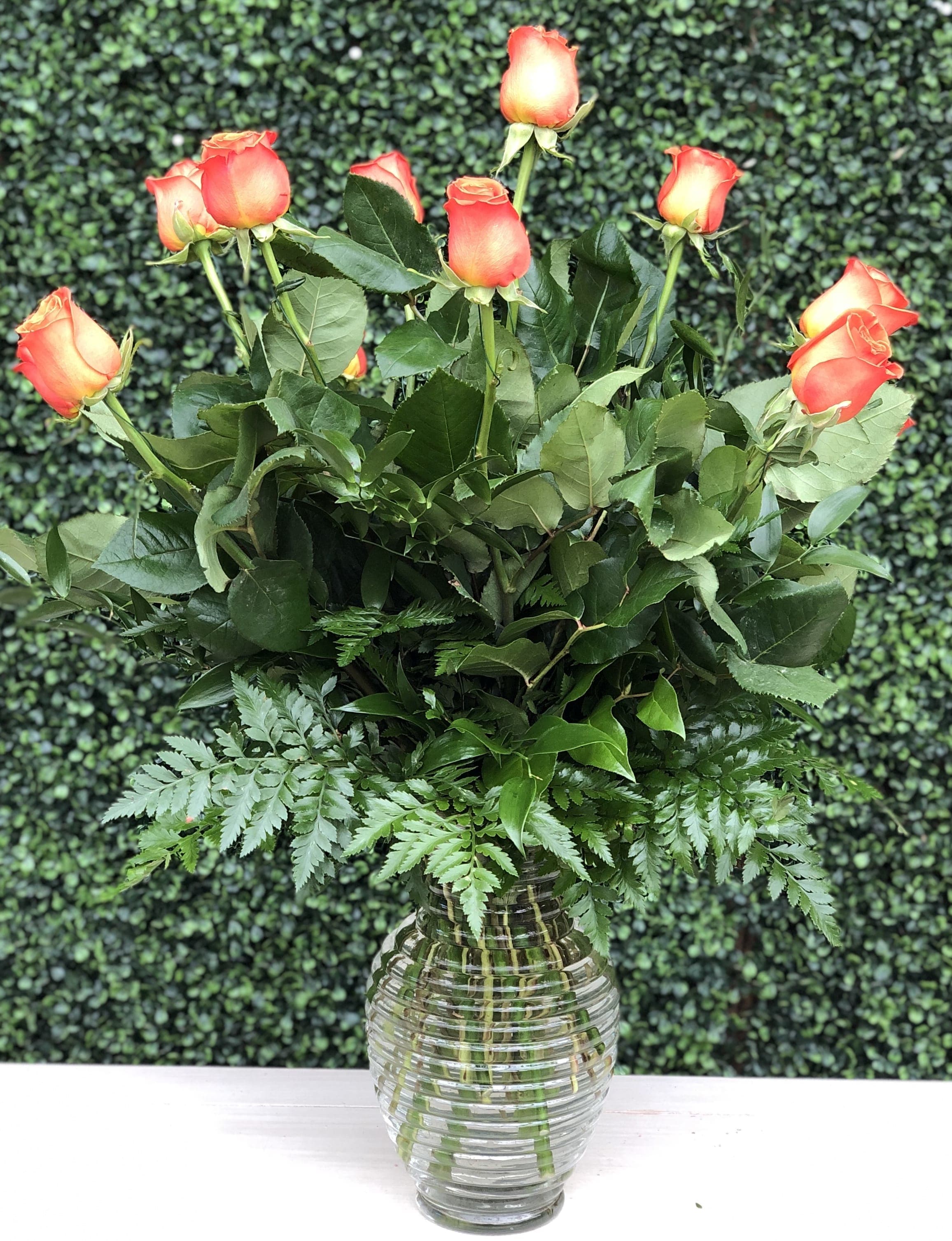 Orange roses arranged in a clear glass vase with fern foliage