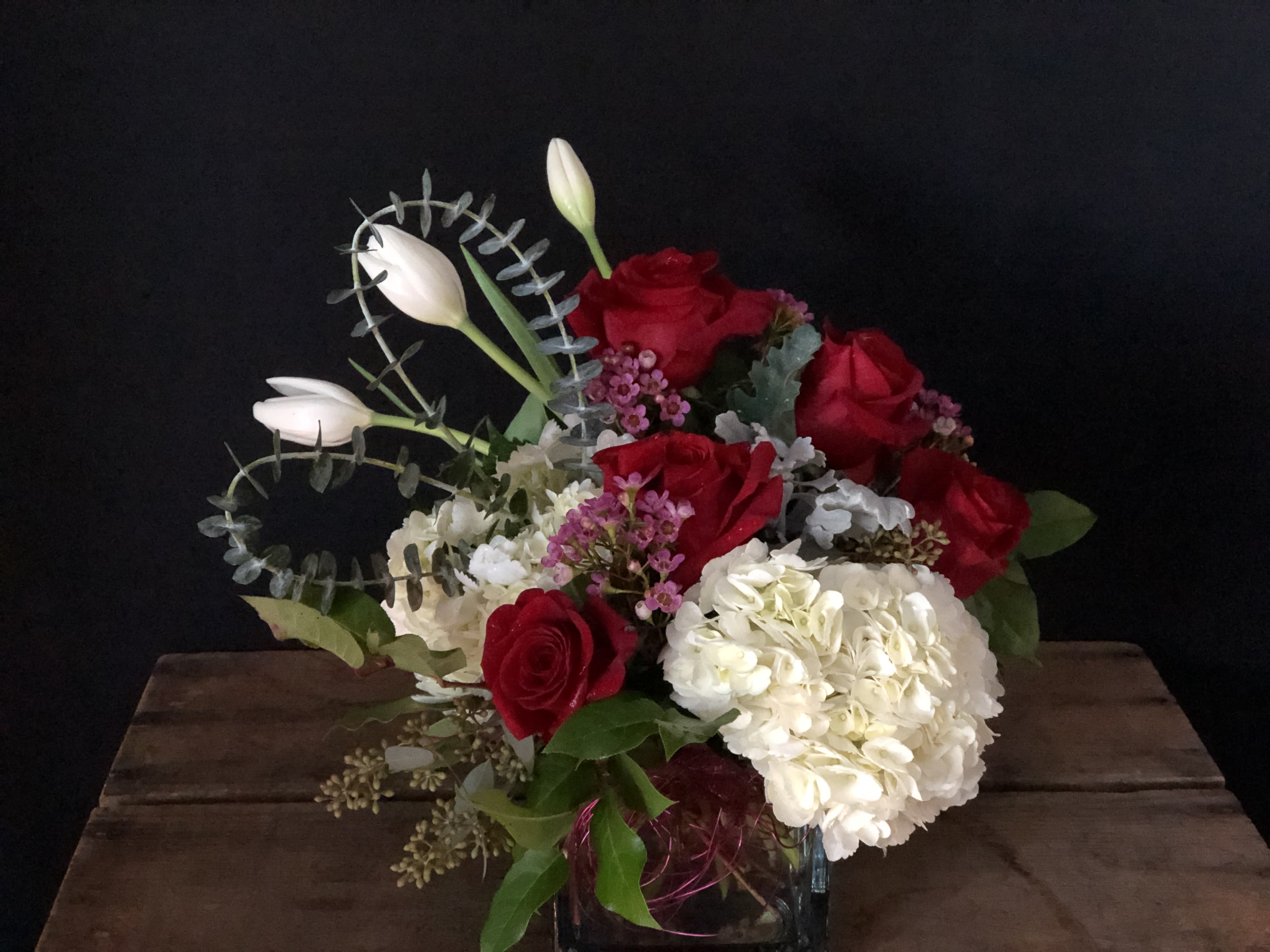 Red roses and white hydrangea in a glass vase with white tulips