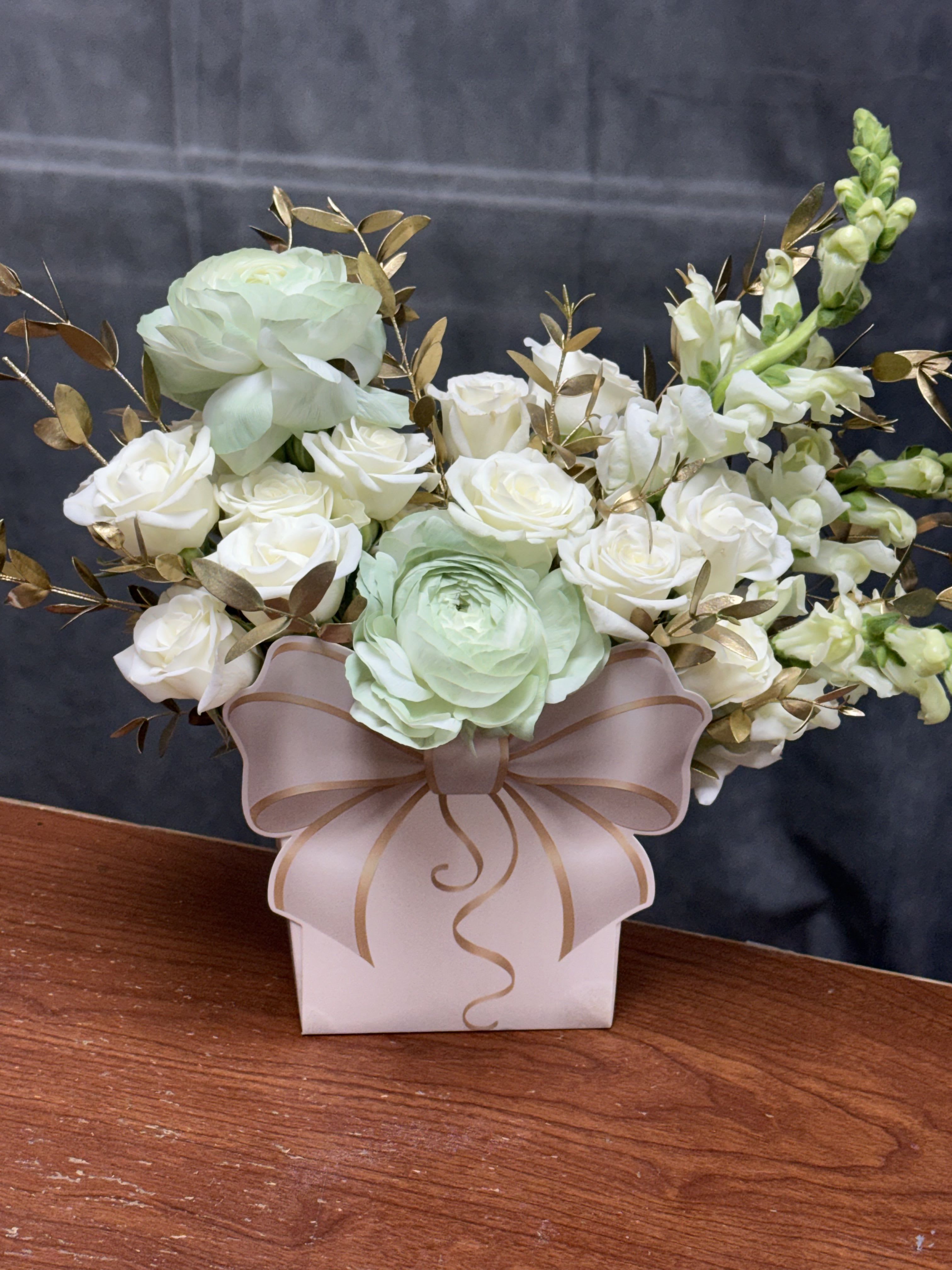 Golden Grace Bow Bag - A luxurious blend of white blooms, soft green ranunculus , and gold-tinted greenery beautifully presented in a stylish bow-shaped paper bag. Designed to bring sophistication and joy to any occasion.