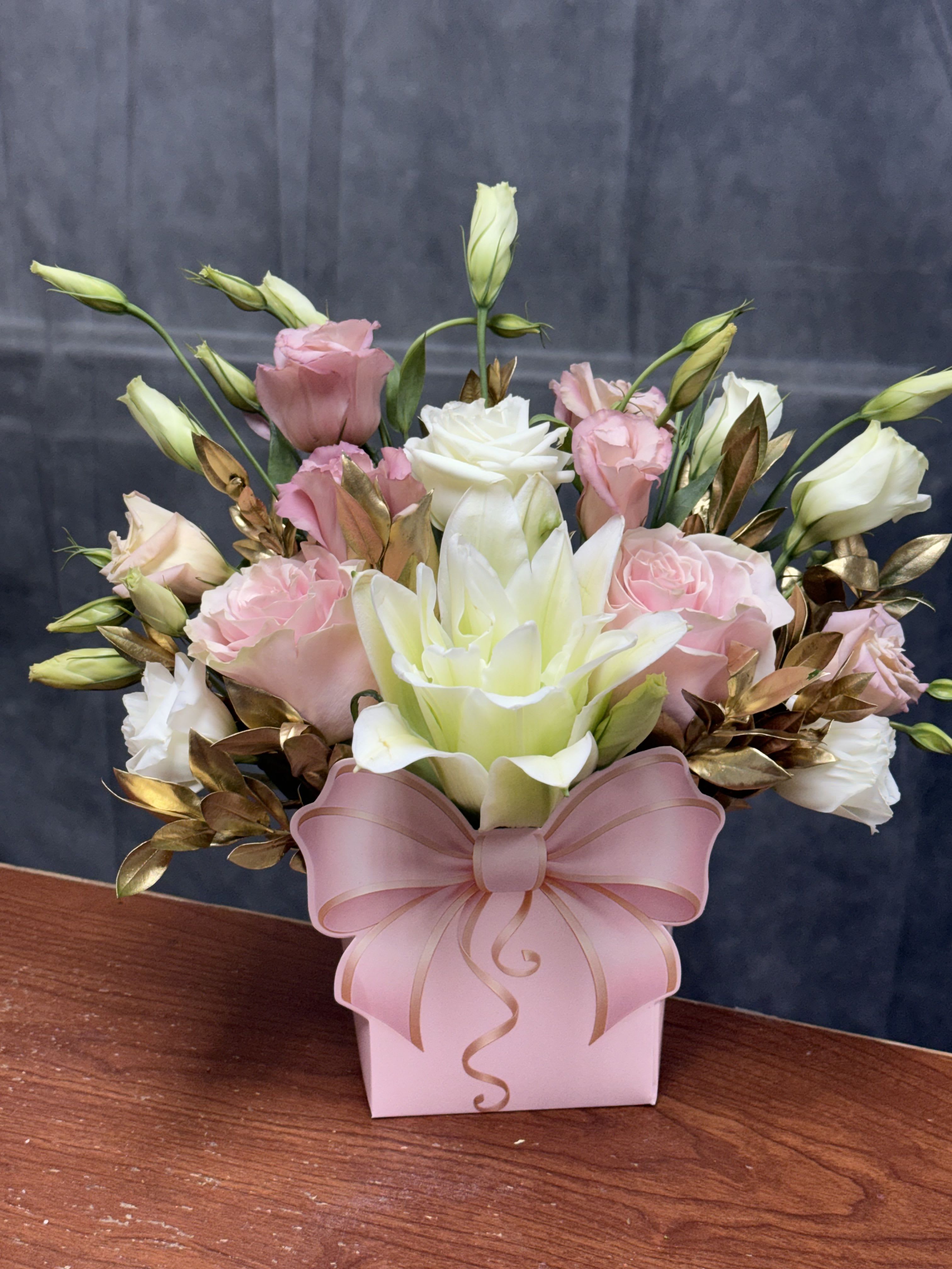 Blush and Gold Bow Bag - A luxurious arrangement featuring blush roses, white lilies, and golden foliage for an unforgettable presentation! Made in paper bag. 