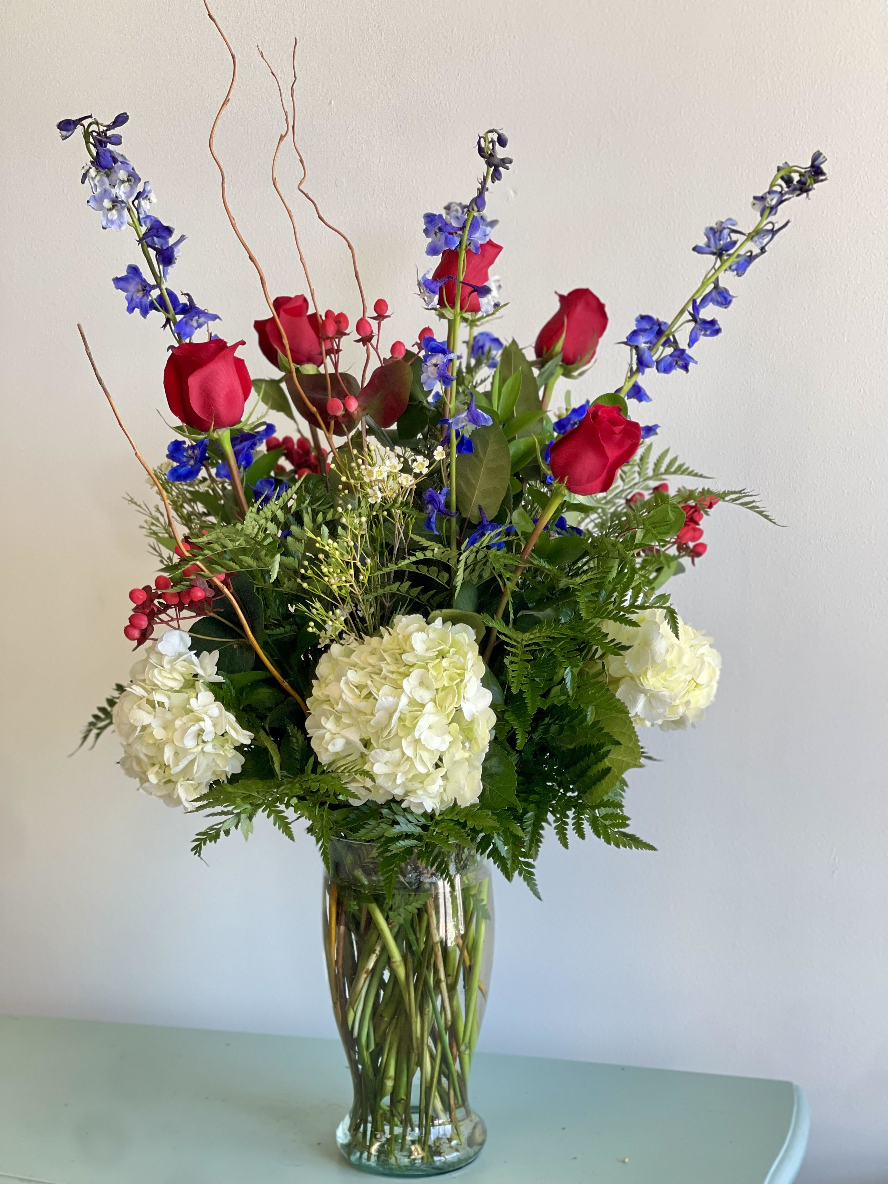 Tall bouquet of red roses, white hydrangeas, and blue flowers in a glass vase