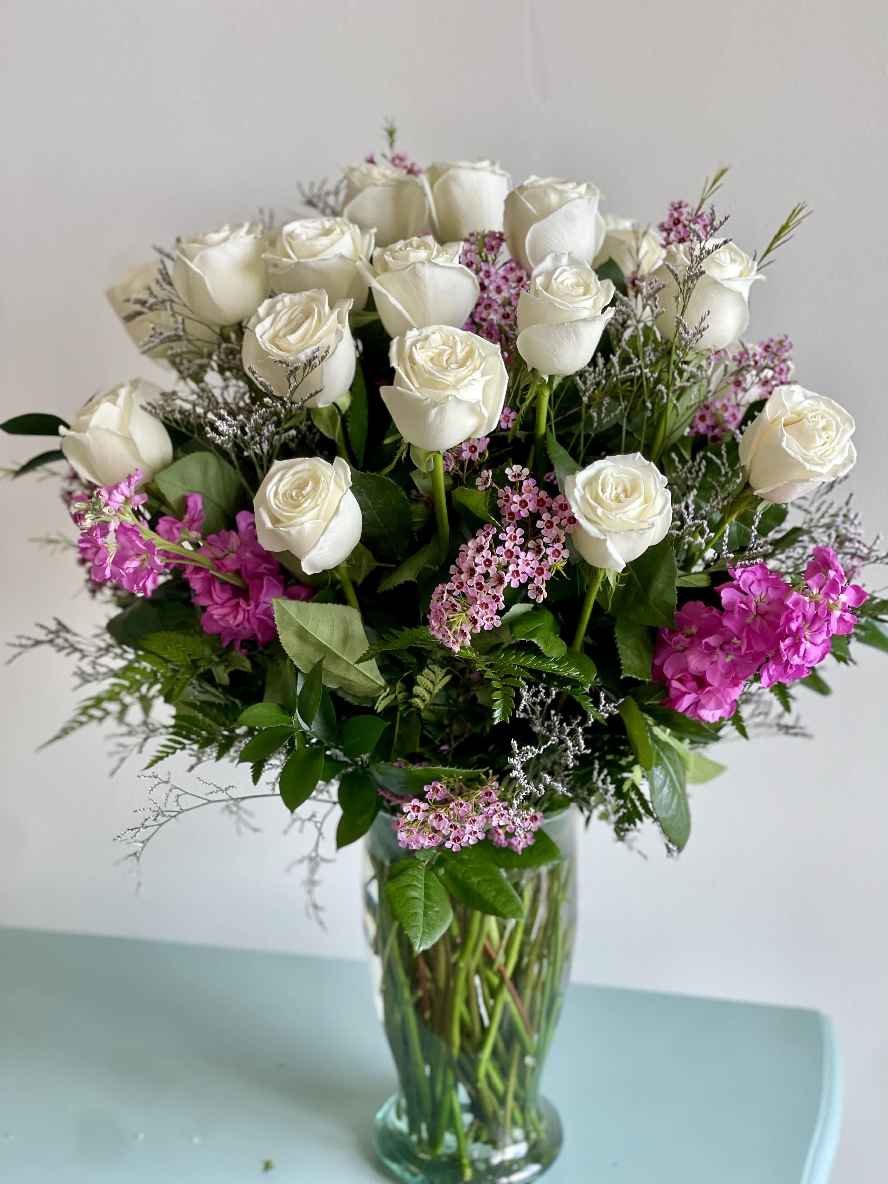 White roses and pink filler flowers arranged in a clear glass vase