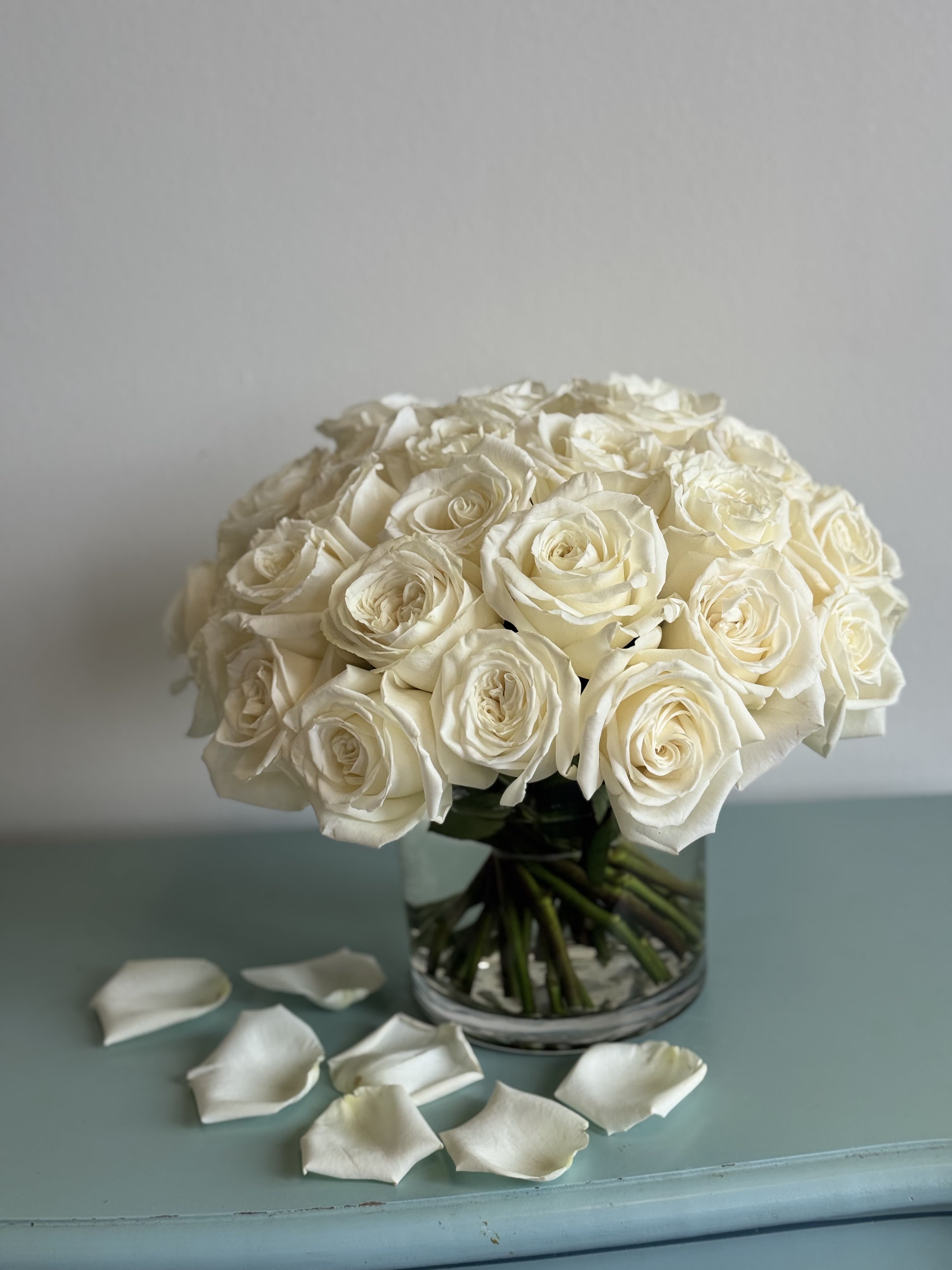 Bouquet of white roses in a clear glass vase with scattered petals
