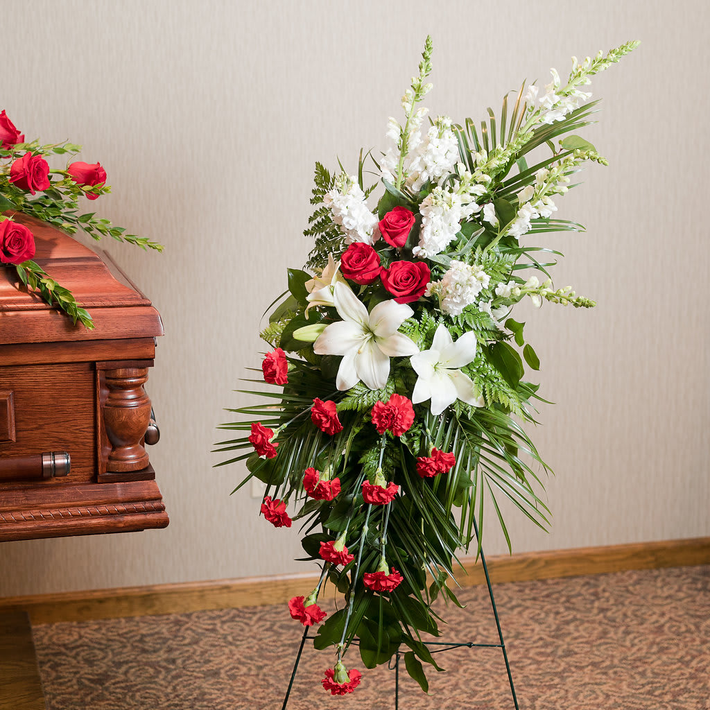 Standing funeral spray with red and white flowers beside a casket