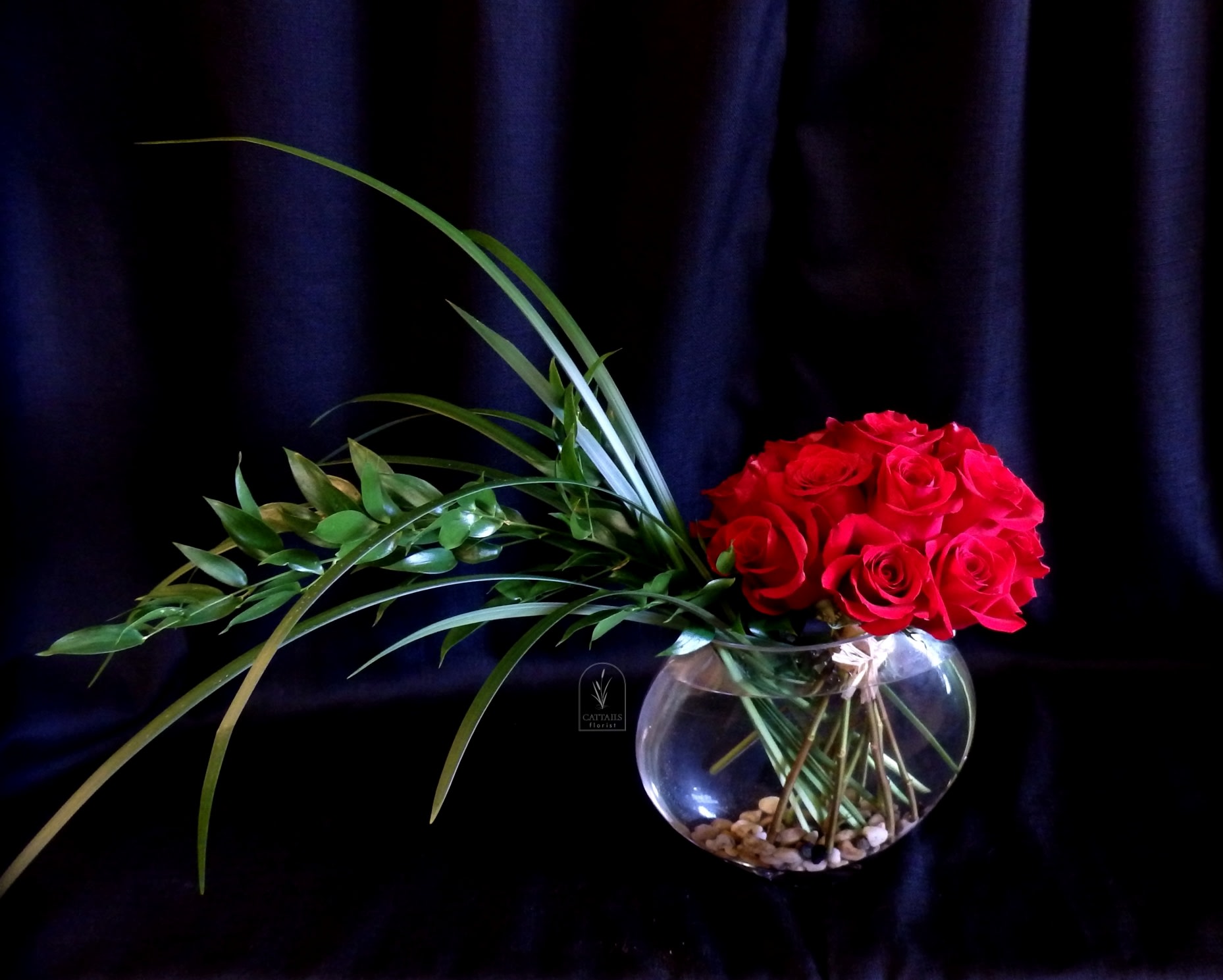 Red roses arranged in a round glass vase with long green leaves