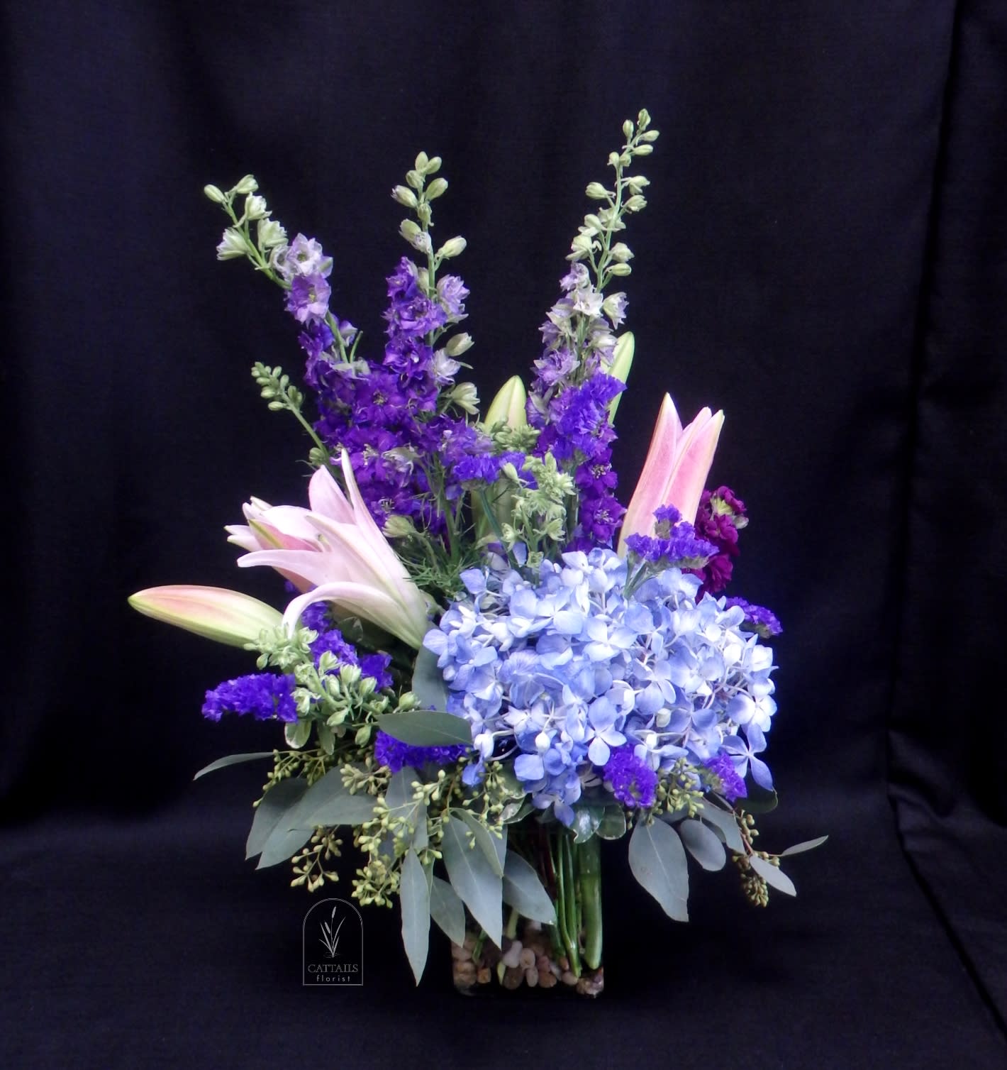 Purple and blue floral arrangement with lilies and hydrangeas in a glass vase
