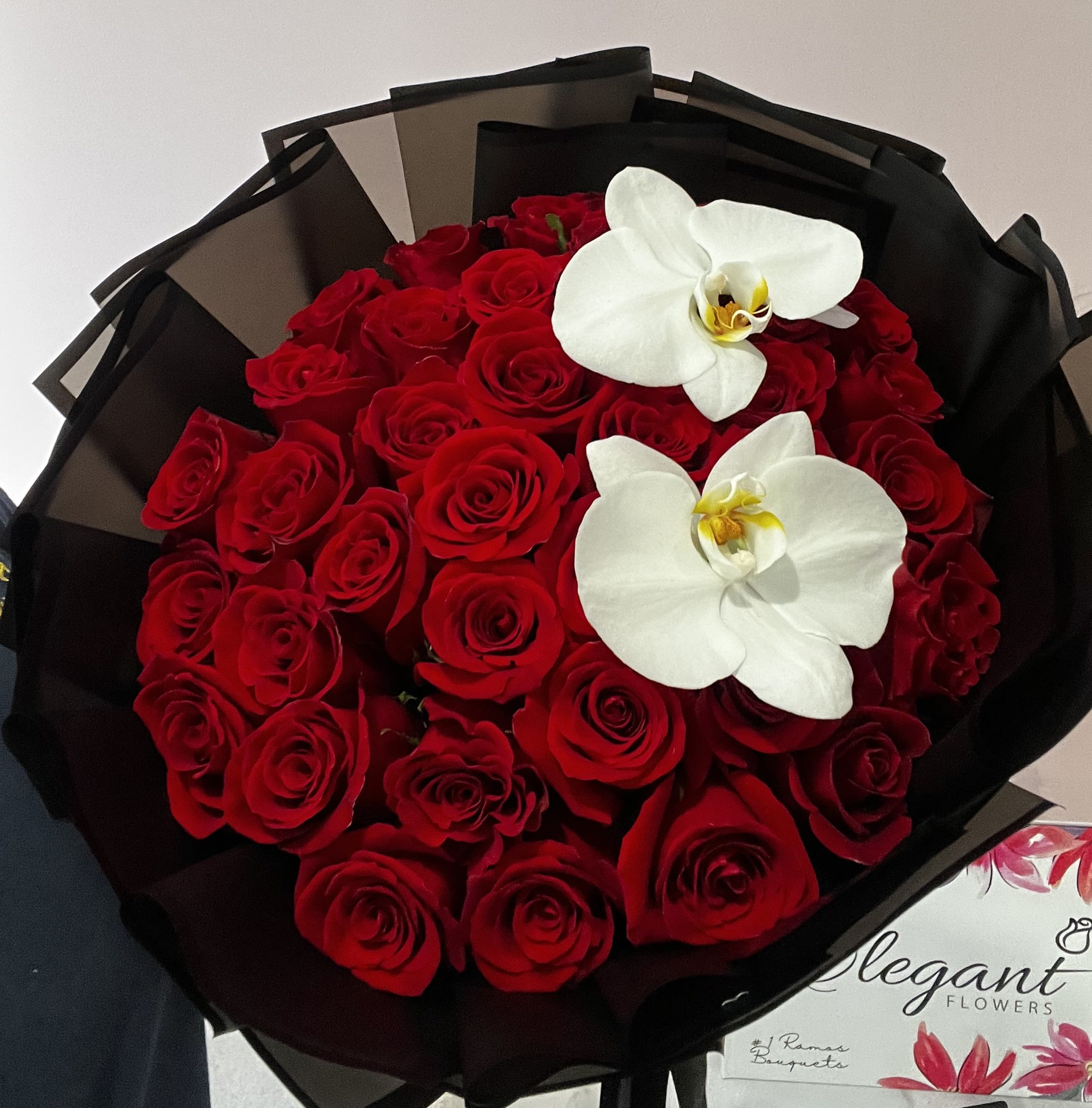 Bouquet of red roses with two white orchids wrapped in black paper