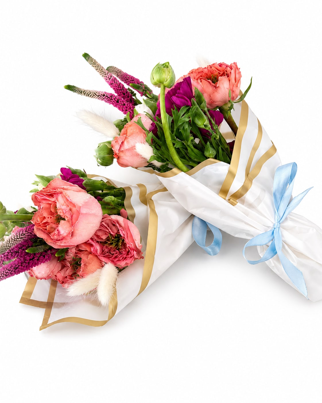 Mini Bouquet  - Coral and pink carnations mingle with upright purple spikes and soft white feathery accents in this cheerful mini bouquet - a bright, romantic hand-tied arrangement perfect for a birthday, anniversary, or a just-because spring surprise. The compact size and playful color mix (pink, purple, white, peach) create an immediate feeling of celebration; the person you're sending it to will feel seen and delightfully spoiled the moment they unwrap it.  Each mini bouquet is wrapped in white paper with elegant gold edging and finished with pale blue and gold ribbons for a charming, gift-ready presentation. The stems include tulip accents and other seasonal blooms that add texture and height, while the feathery whites lend an airy contrast to the richer coral and magenta tones. Small and sweet, it's ideal for desks, bedside tables, or a cozy kitchen vase.  Made to arrive ready-to-gift, these hand-tied bouquets require minimal care - trim stems and refresh water every couple of days to keep them perky. Choose this mini bouquet when you want a compact, joyful arrangement that says "I'm thinking of you" with color and whimsy.