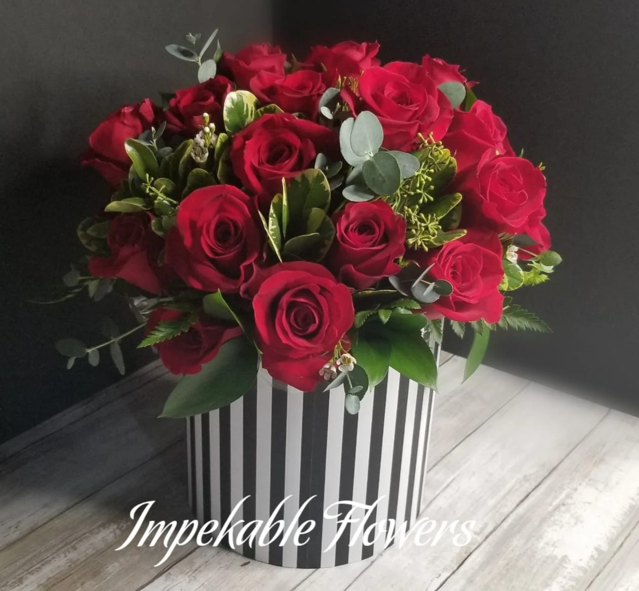 Round arrangement of red roses in a black and white striped cylinder box
