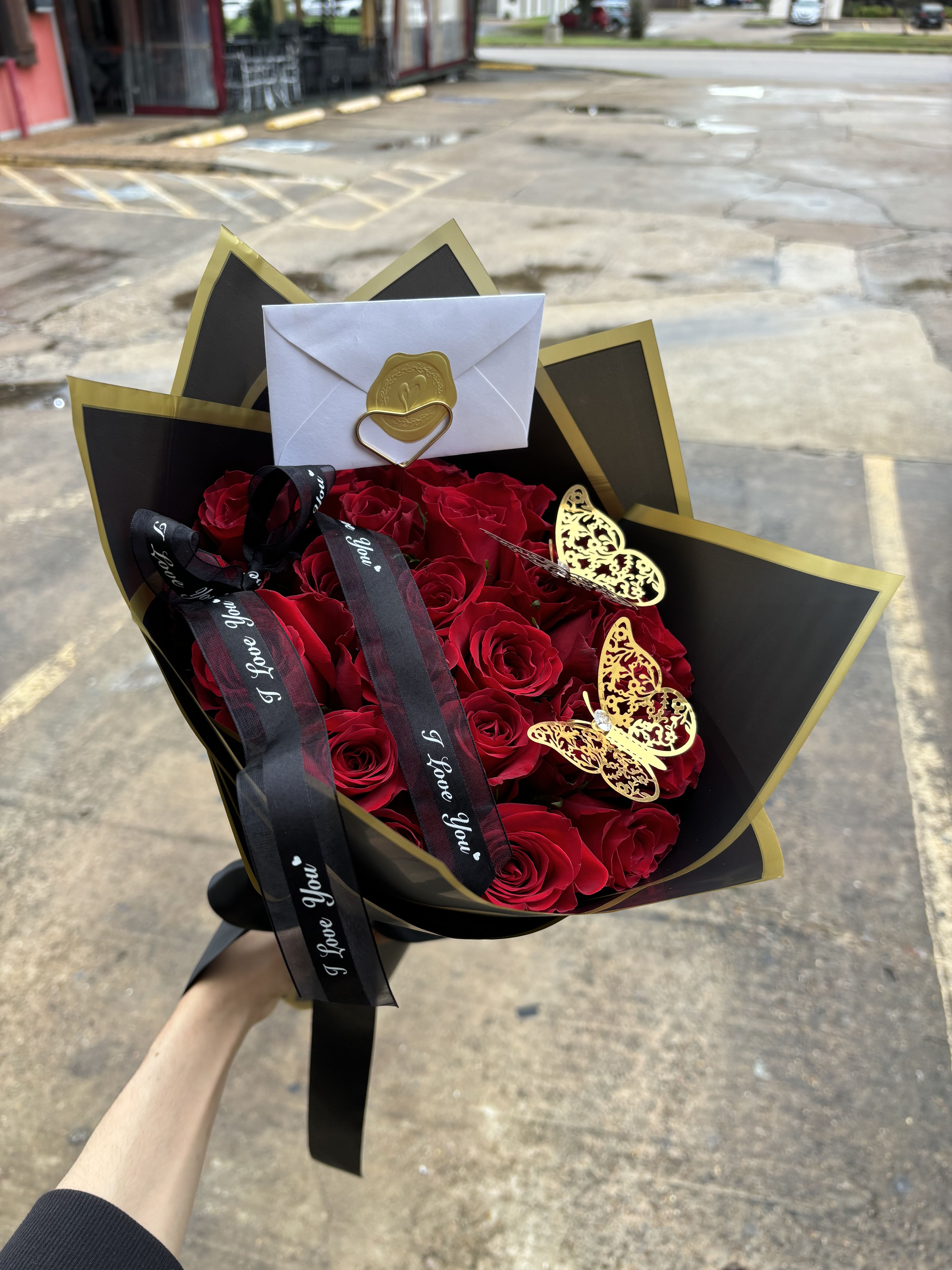 Bouquet of red roses wrapped in black and gold paper with ribbons and butterfly accents