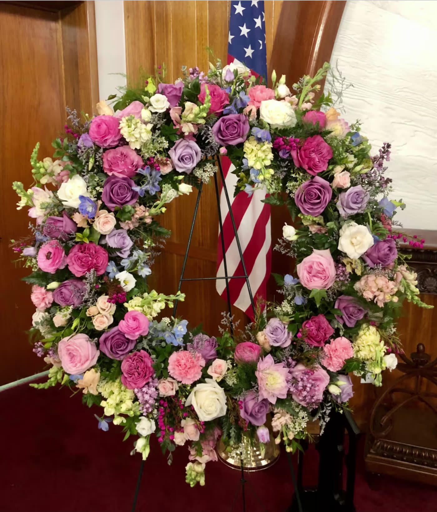 Large floral wreath of pink, purple, and white flowers on a stand