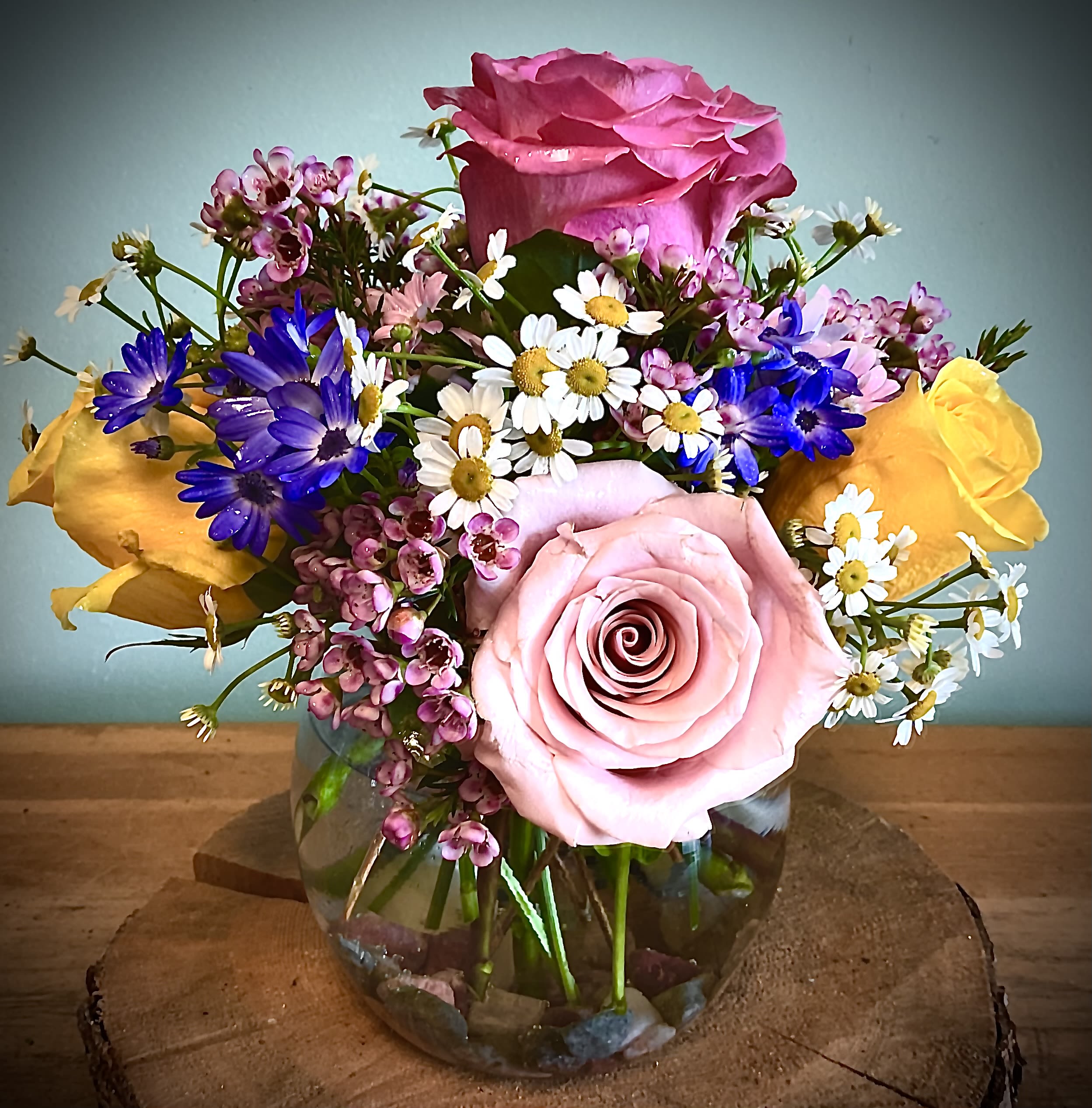 Mixed bouquet of pink and yellow roses with small daisy flowers in a glass vase