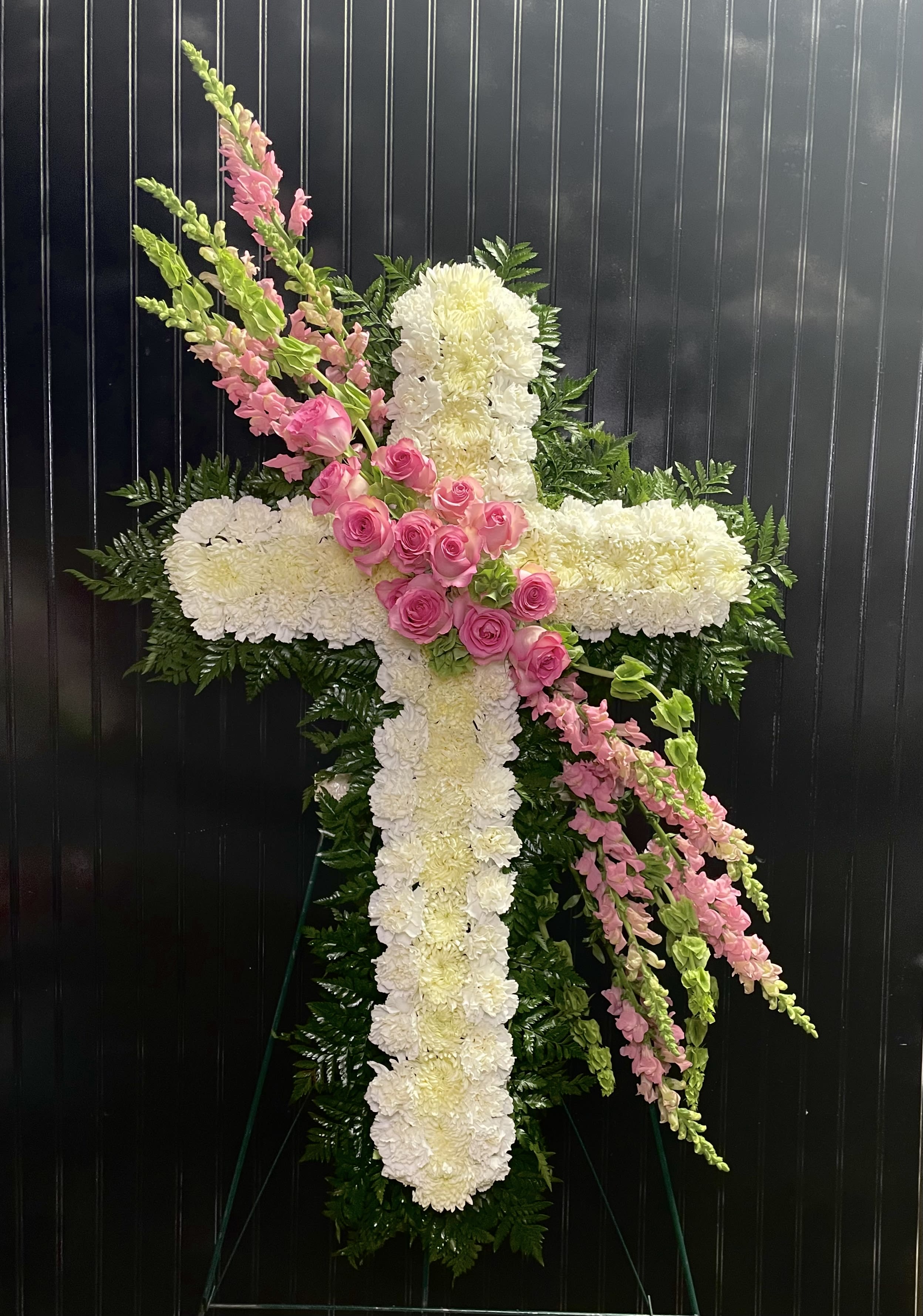 White floral cross with pink roses and snapdragons on a dark background