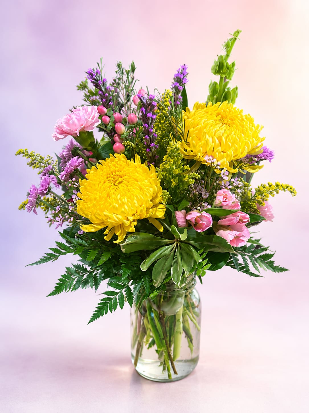 Golden Daydream - Bright, cheerful, and full of whimsical charm, Golden Daydream captures the warmth of a sunlit garden in bloom. Featuring radiant golden spider mums, delicate pink spray roses and carnations, playful pink hypericum berries, airy purple statice, and touches of golden solidago nestled among lush greenery, this arrangement is designed in a clear glass vase with a natural, gathered-from-the-garden feel.  Overflowing with vibrant color and graceful texture, Golden Daydream brings happiness and beauty to any occasion. Whether celebrating a birthday, sending encouragement, or simply brightening someone's day, this joyful bouquet is a reminder that even the simplest moments can feel like sunshine.