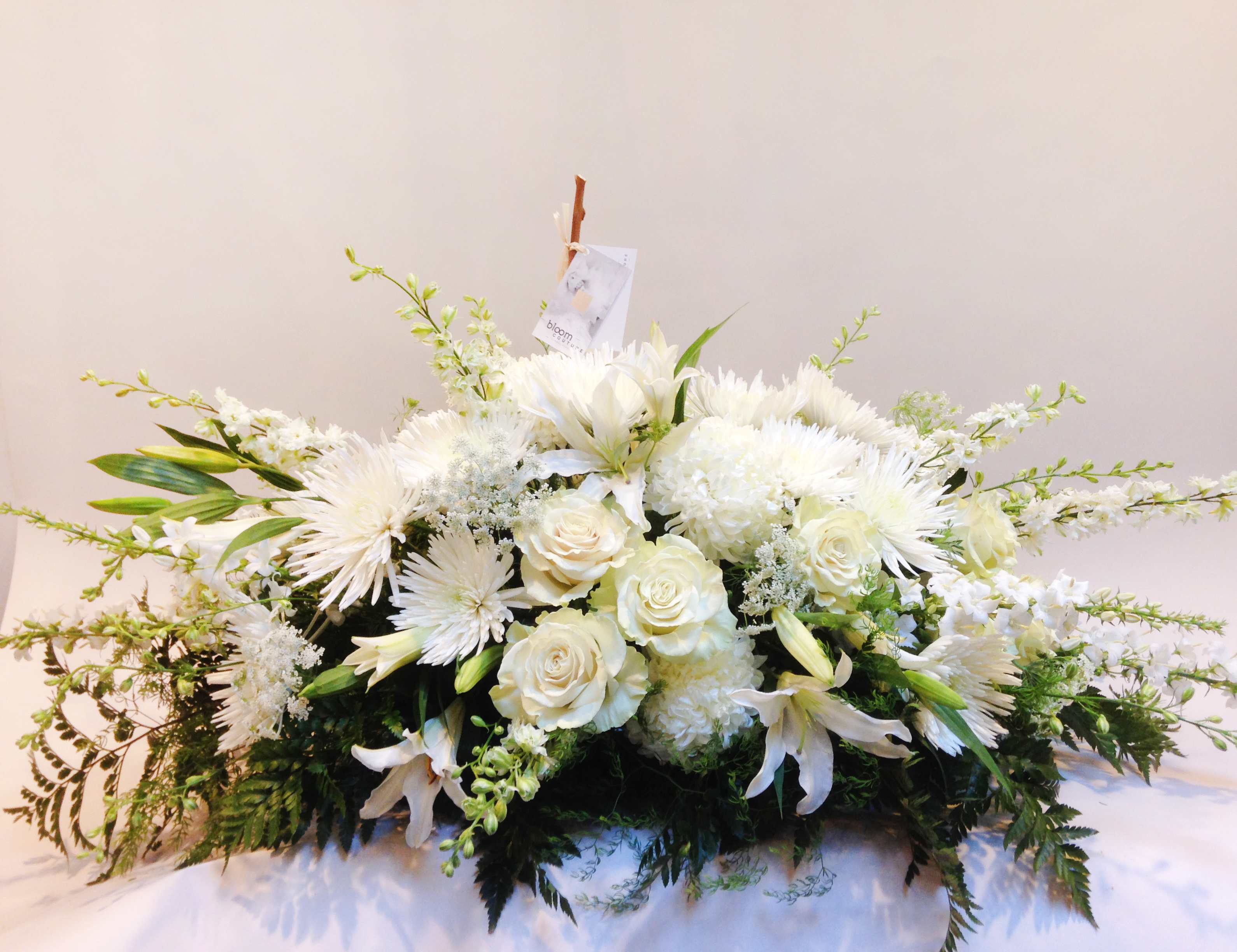 White floral casket spray with roses, lilies, and chrysanthemums
