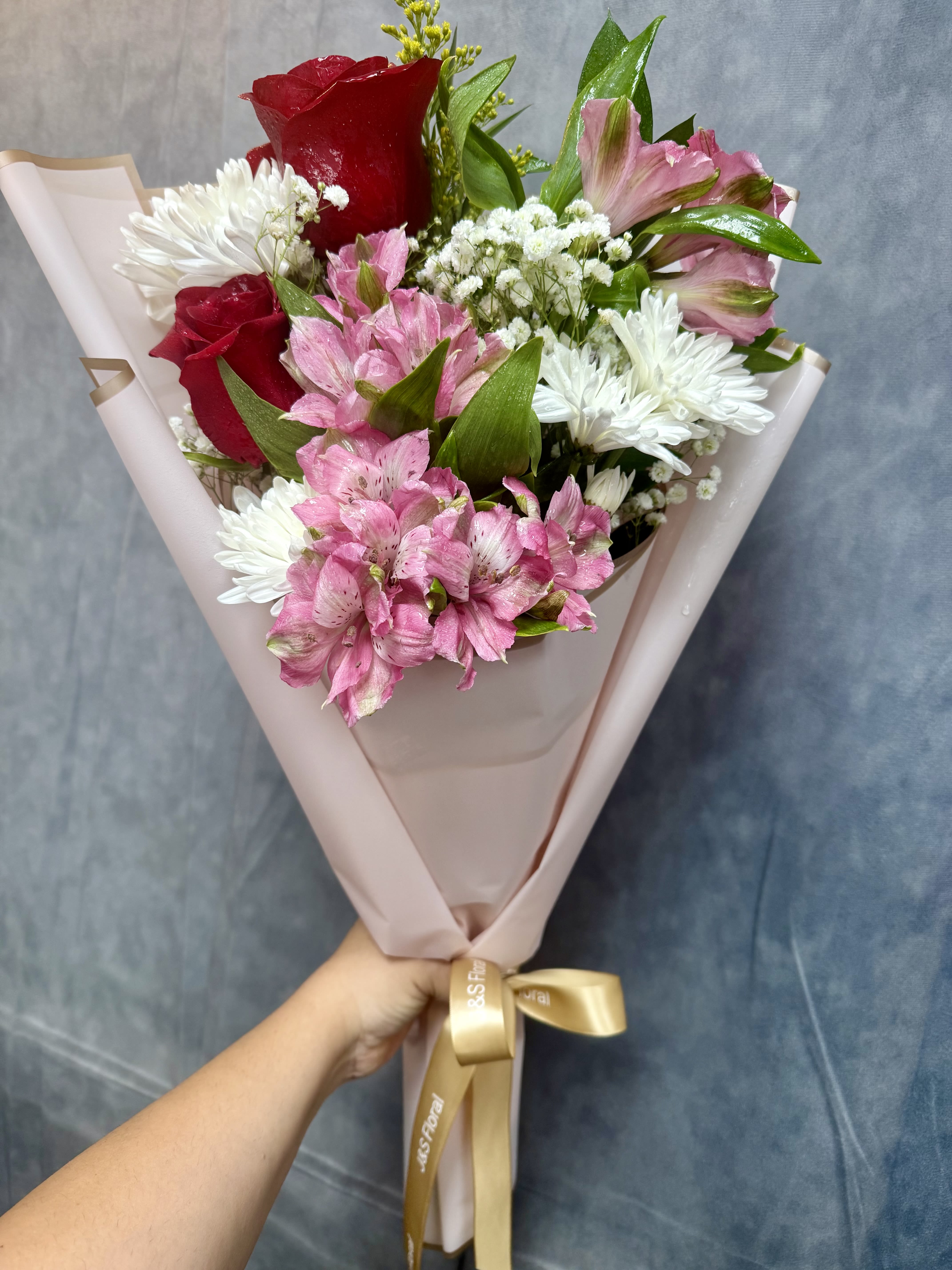 Bouquet of red roses, pink alstroemeria, and white daisies wrapped in blush paper