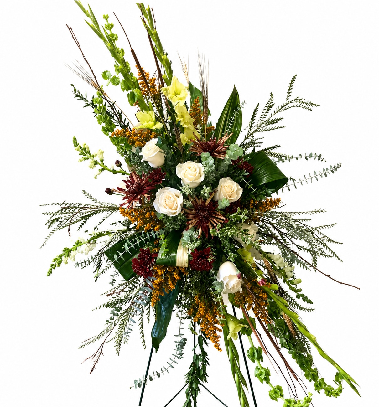 Thoughts of You Standing Spray - A large, upright standing spray that makes a respectful, woodsy statement for sympathy or memorial services. The Woodsy Standing Spray presents cream-white roses at its dense heart alongside burgundy chrysanthemum-like blooms, tall green spikes, and warm orange accents - a color palette of white, deep red, green, and orange that reads solemn yet alive for a funeral or remembrance display.  This formal, expansive arrangement is built on a standing easel with floral foam and layered foliage, including decorative palm leaves and long arching stems that create an asymmetrical, dramatic silhouette. Textures range from the soft, round roses to spiky snapdragons and structured chrysanthemums, giving depth and a natural, forest-like feel at a large scale suitable for view-from-a-distance placement in a chapel, memorial, or public event space.  Designed to honor and comfort the person you're thinking of, the spray conveys dignity while recalling the warmth of shared memories. It arrives ready to display on the included easel; keep it in a cool location away from direct sun and replace water at the foam as instructed by the funeral home or venue to preserve freshness during services.