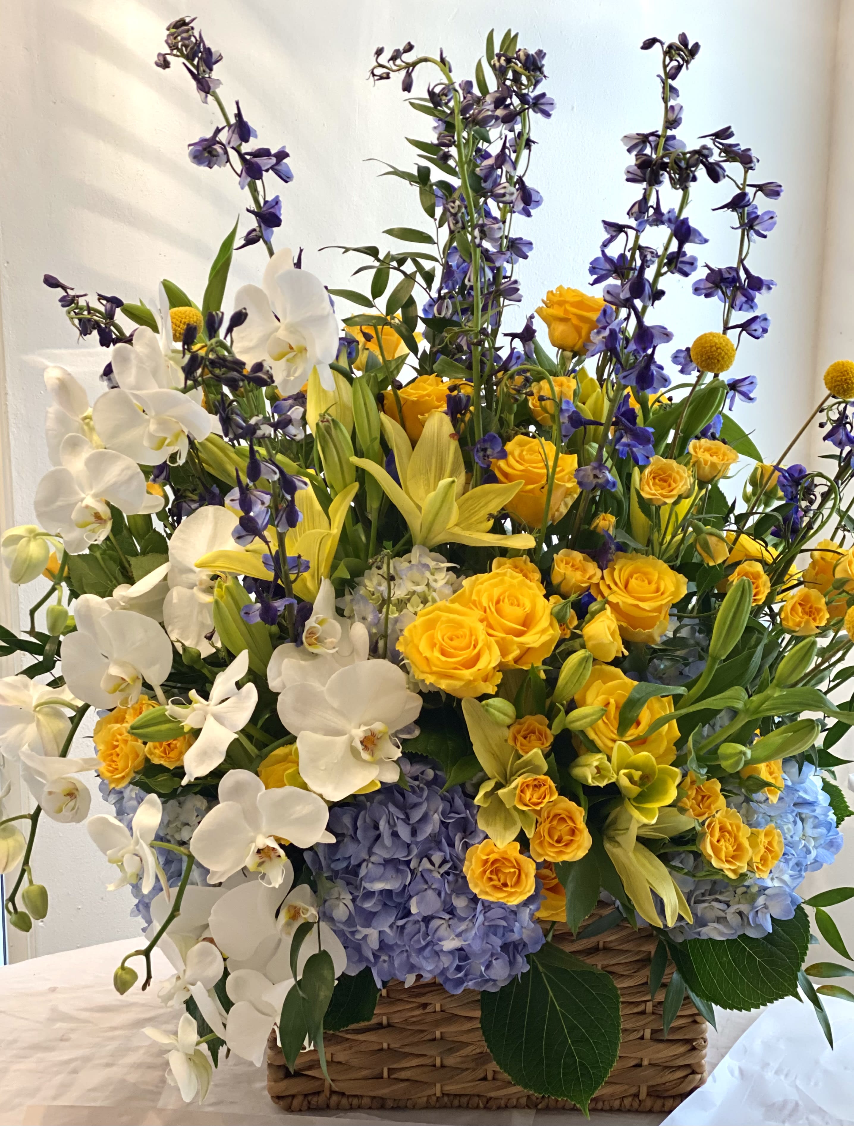 Basket arrangement of white orchids, yellow roses, and blue hydrangeas