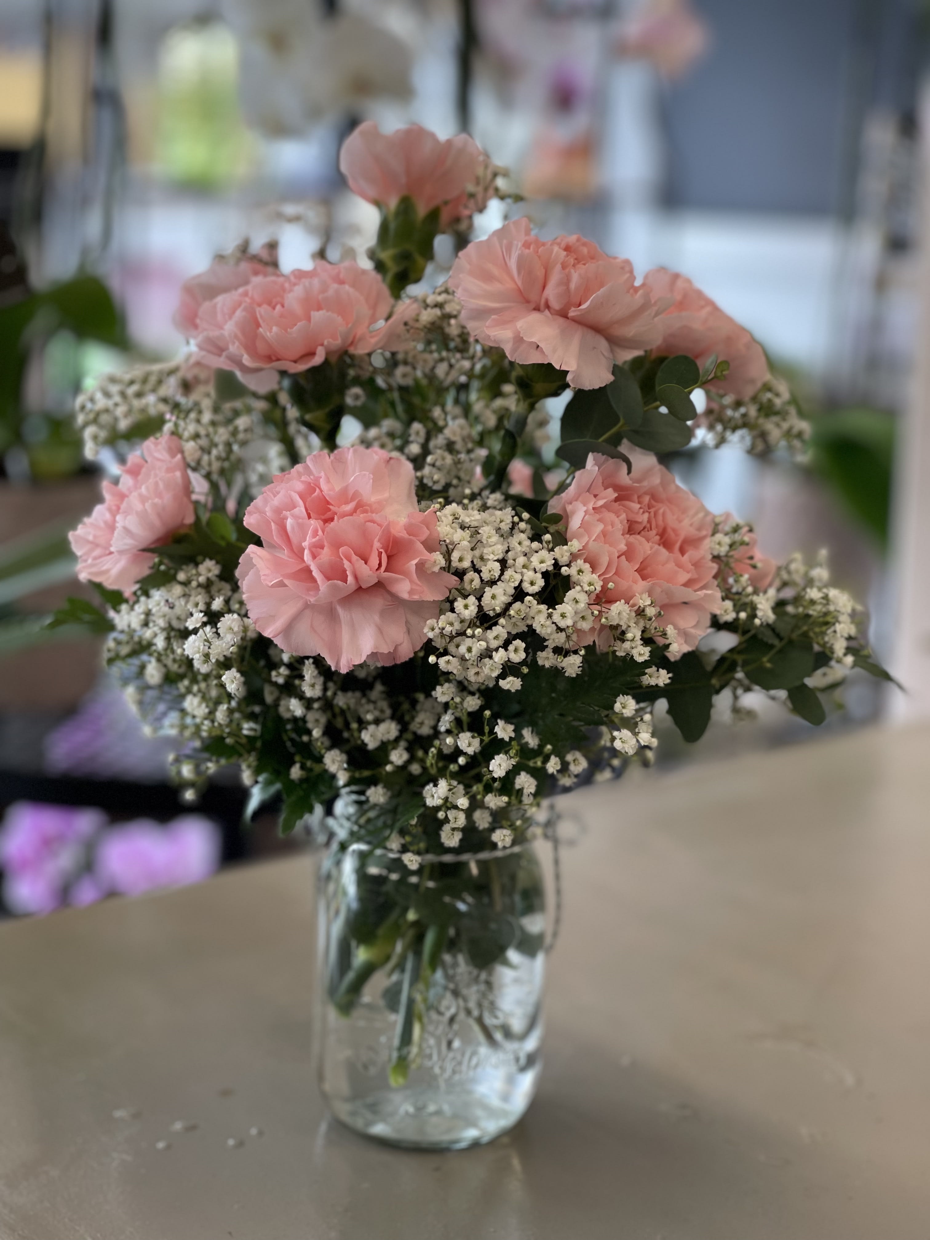 Pink carnation and white filler flower bouquet arranged in a clear glass jar